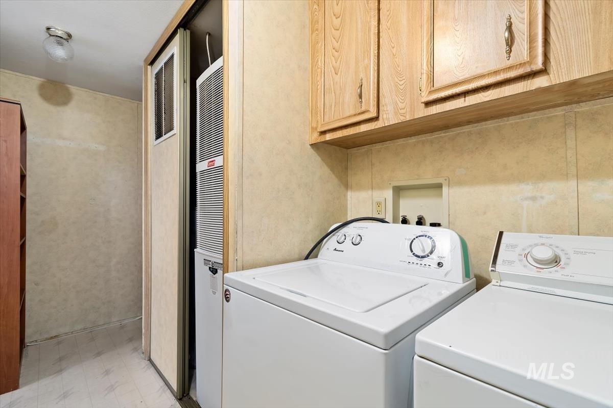 Laundry room with light flooring, washing machine and dryer, a heating unit, and cabinet space