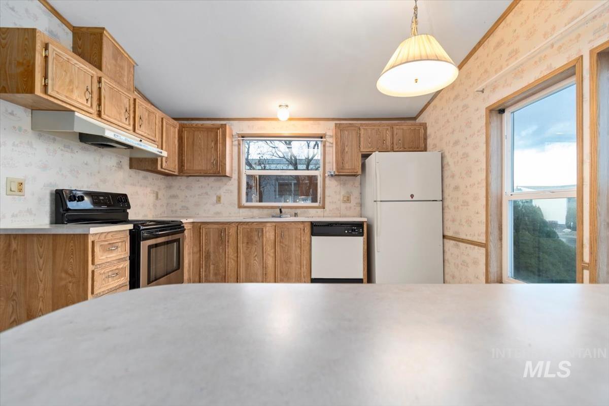 Kitchen with white appliances, wallpapered walls, light countertops, under cabinet range hood, and pendant lighting