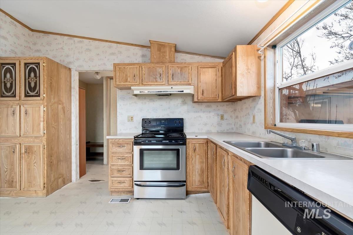 Kitchen with light flooring, stainless steel range with electric cooktop, wallpapered walls, vaulted ceiling, and dishwasher
