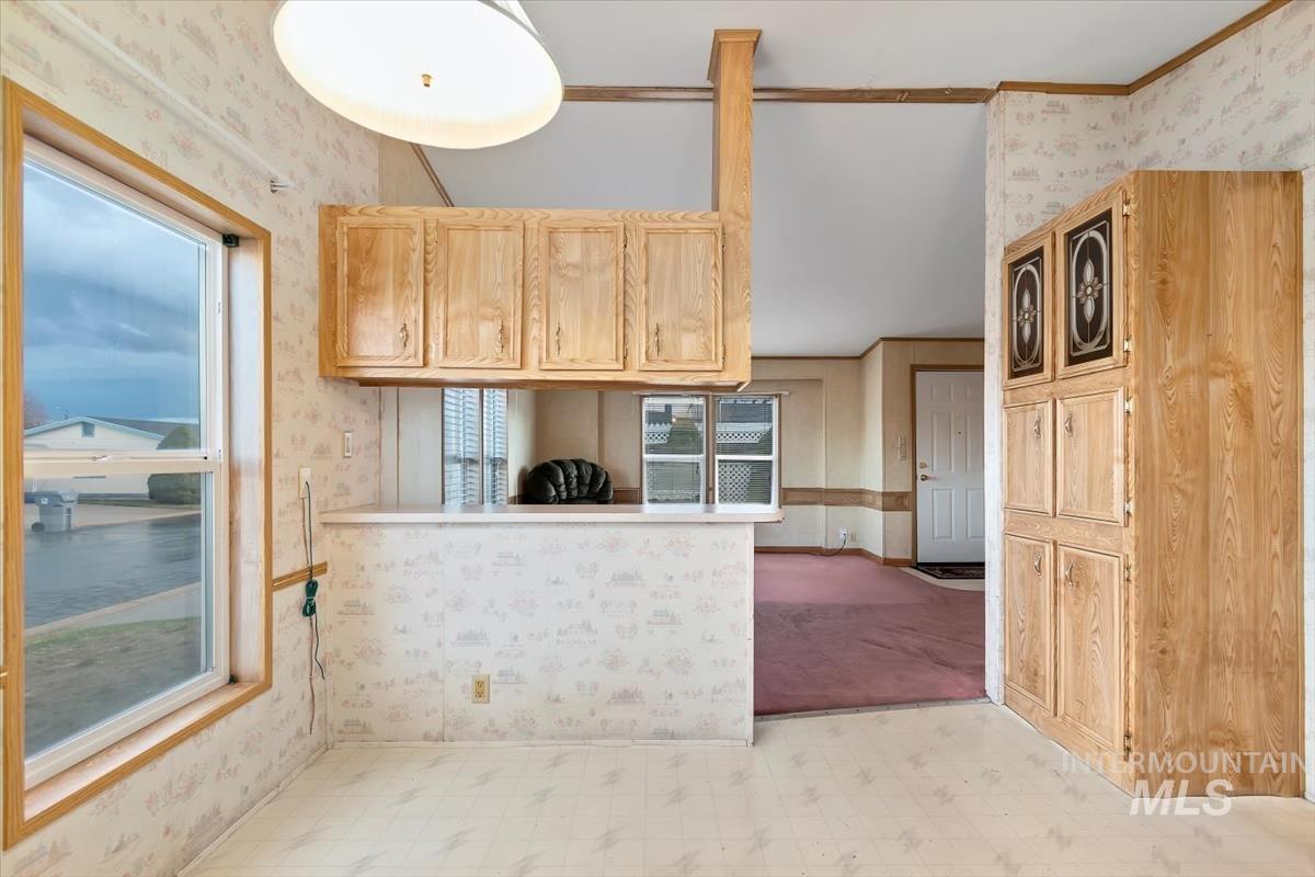 Kitchen with wallpapered walls, light flooring, light brown cabinetry, and plenty of natural light