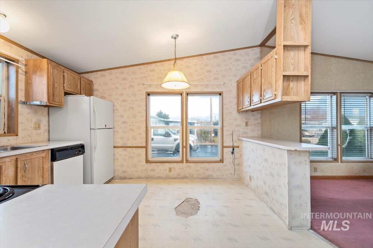 Kitchen with vaulted ceiling, light countertops, wallpapered walls, dishwasher, and decorative light fixtures