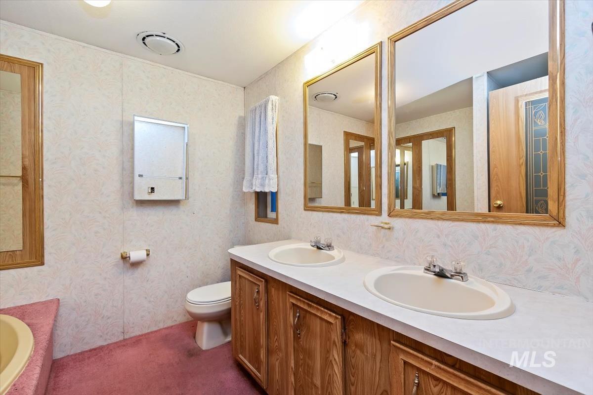 Bathroom featuring double vanity, wallpapered walls, a tub to relax in, and dark colored carpet