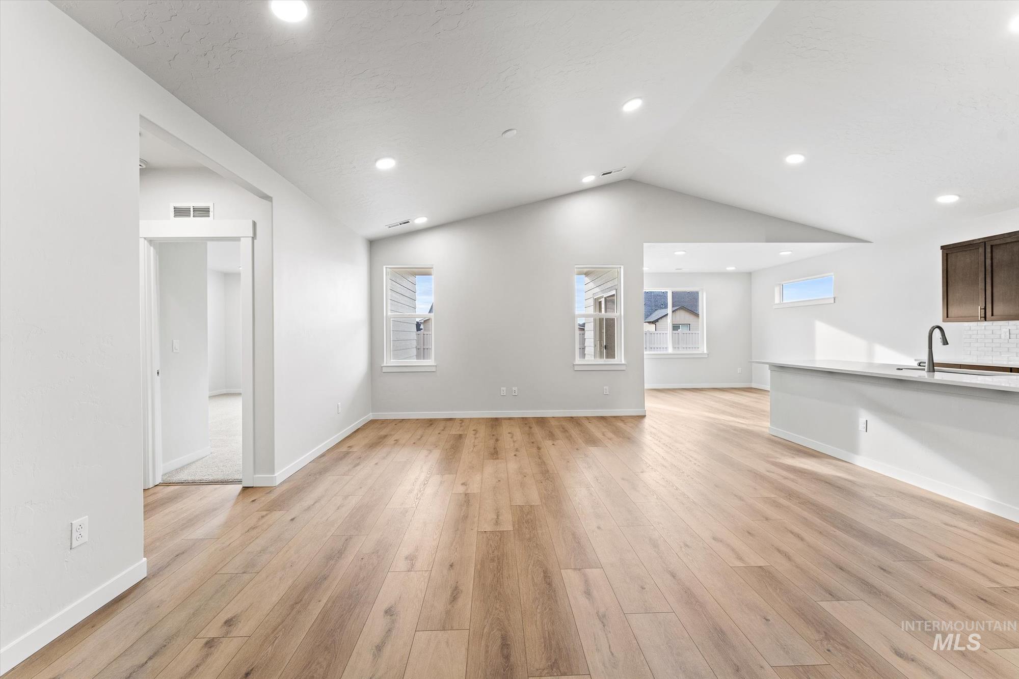 Unfurnished living room with light wood finished floors, vaulted ceiling, and recessed lighting