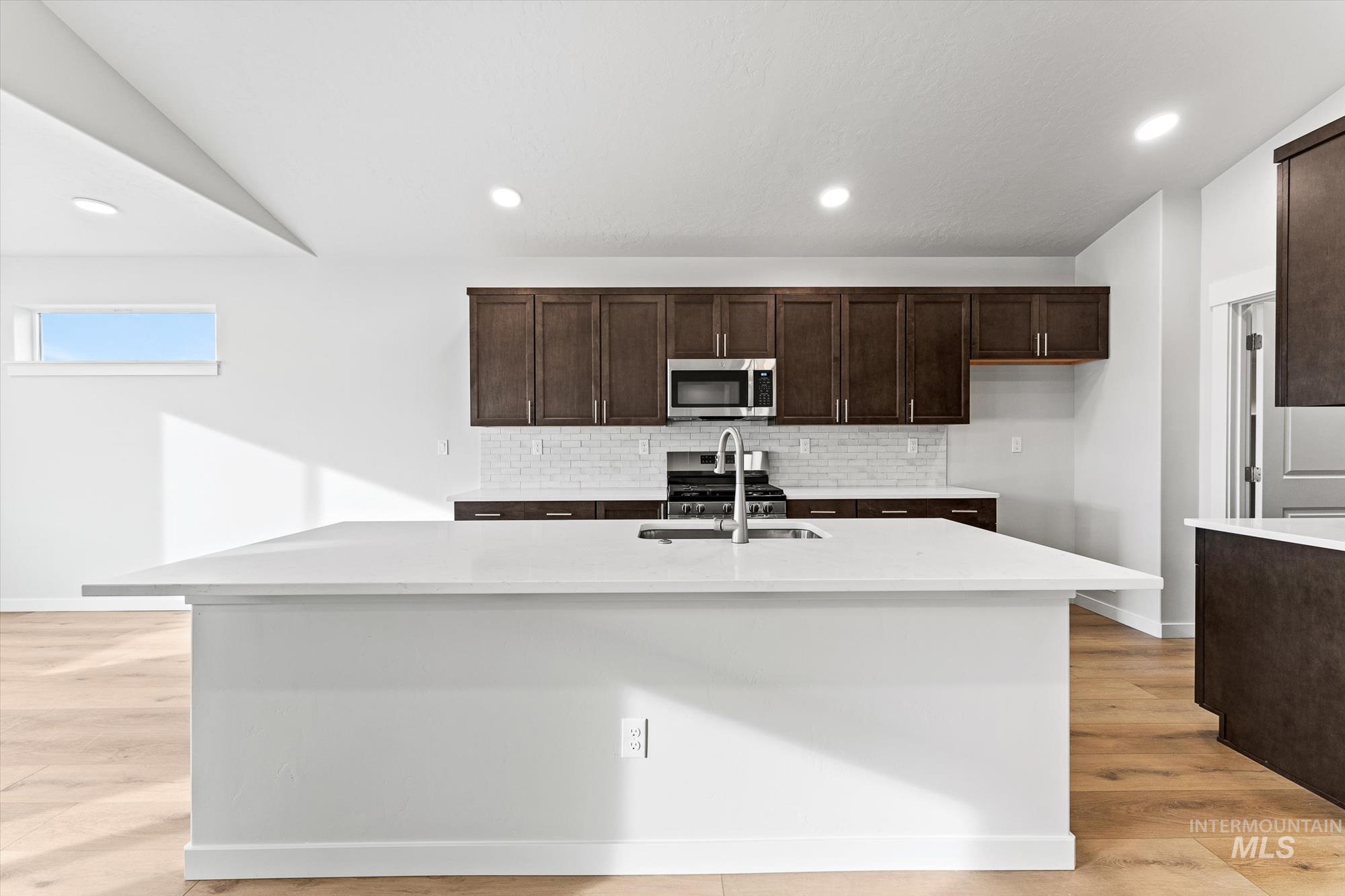 Kitchen featuring dark brown cabinets, tasteful backsplash, light wood-style flooring, recessed lighting, and a center island with sink