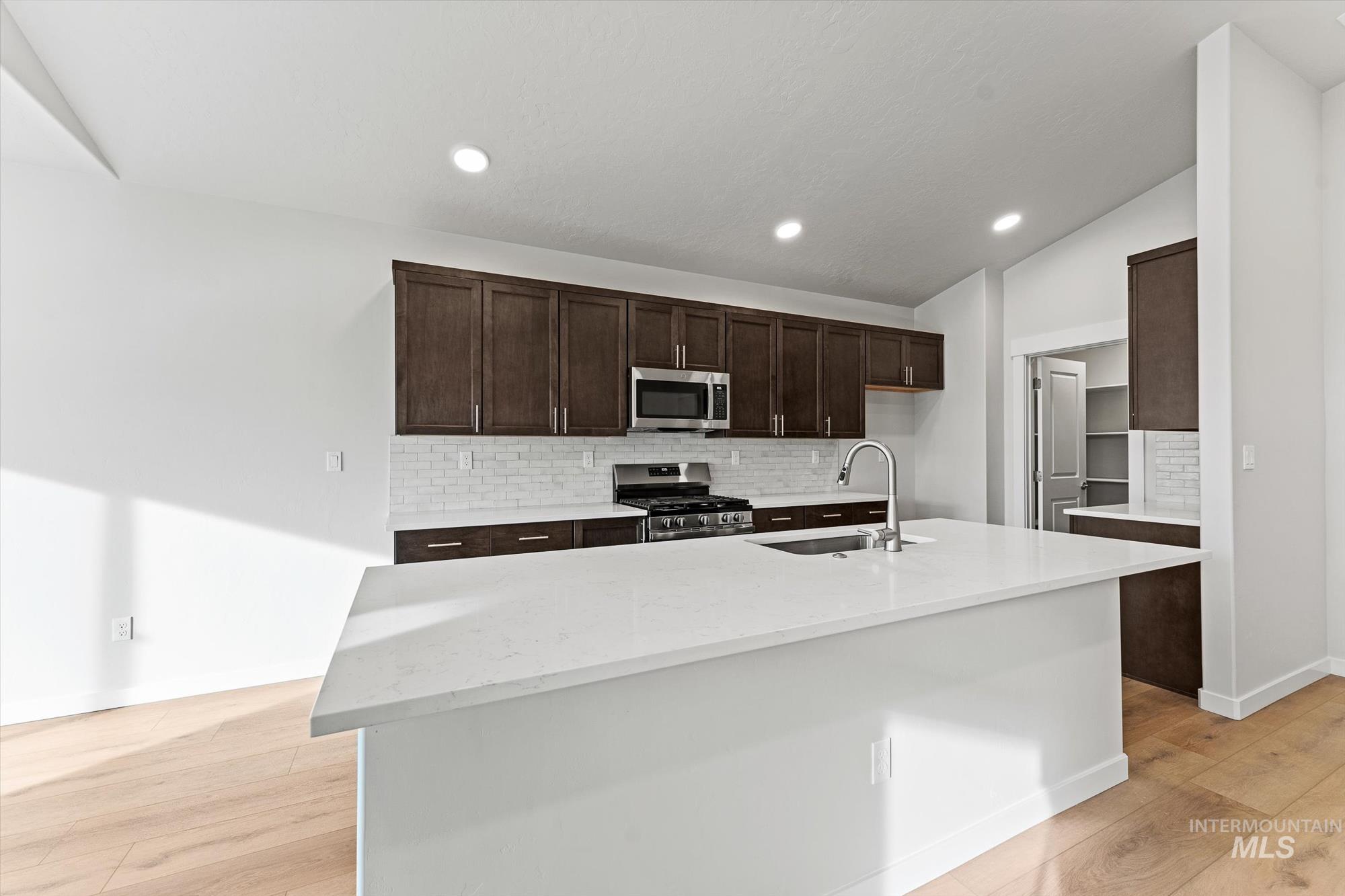 Kitchen featuring backsplash, stainless steel appliances, light stone counters, dark brown cabinets, and recessed lighting