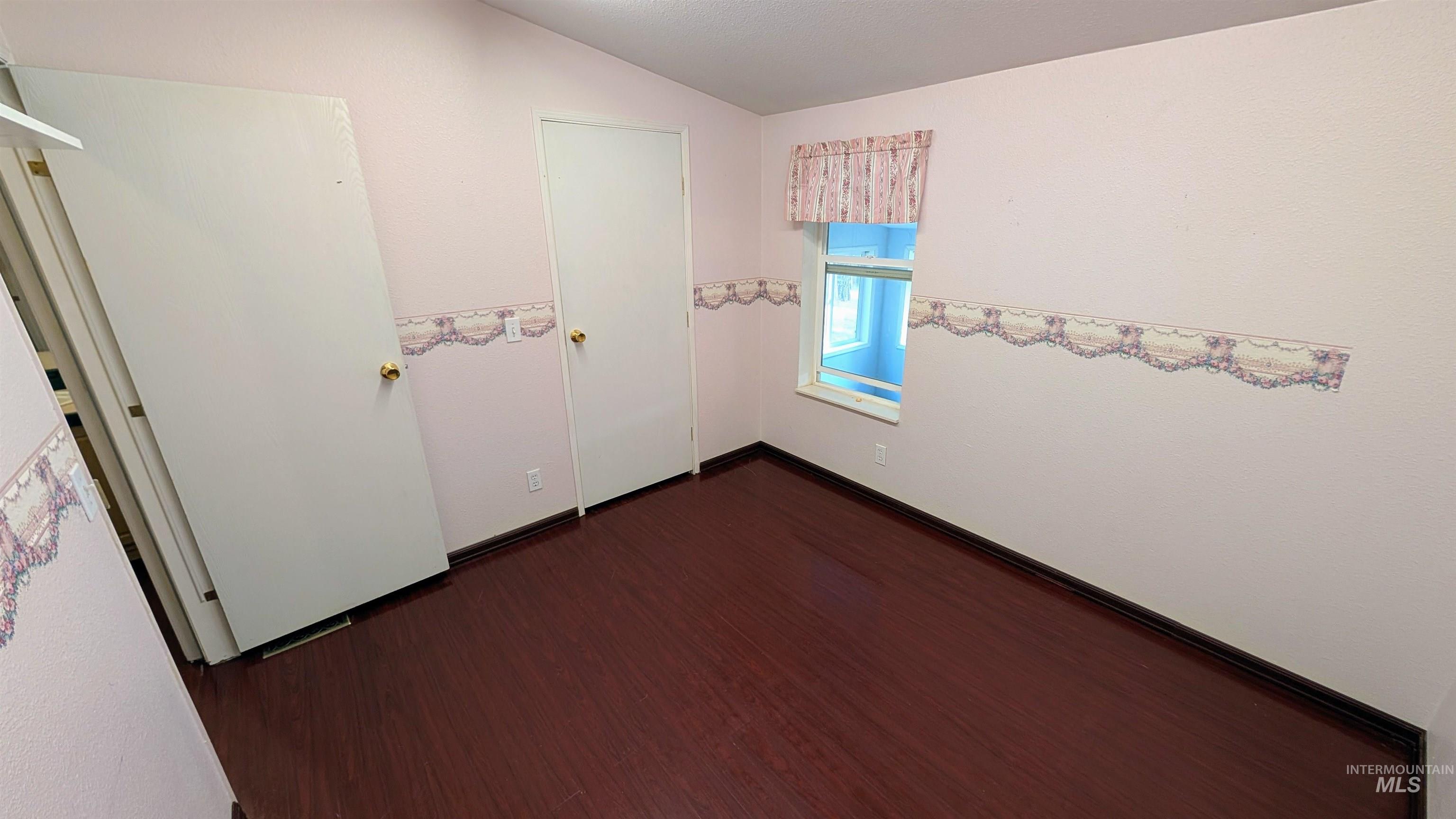 Unfurnished bedroom featuring dark wood finished floors and vaulted ceiling