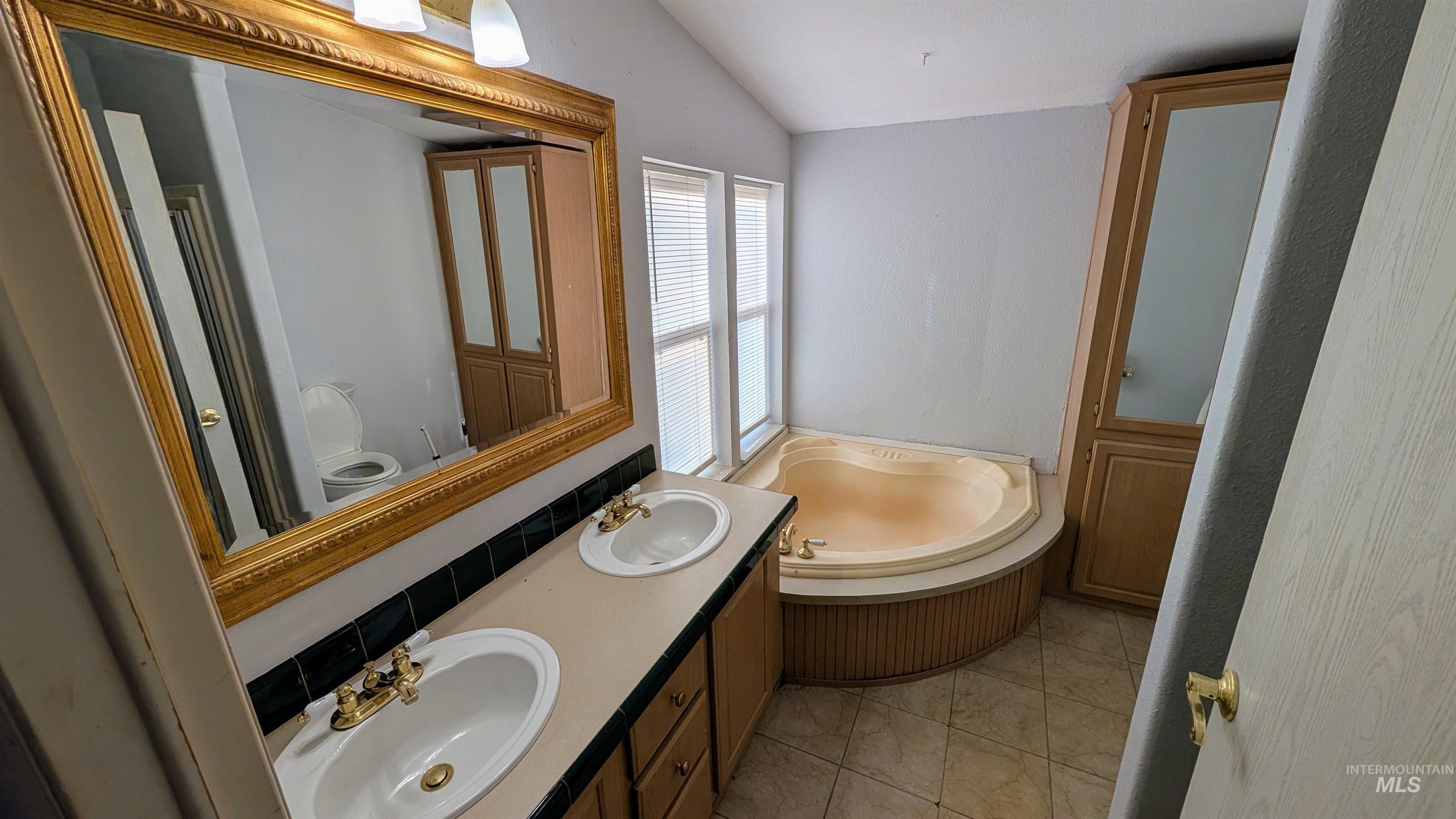 Full bathroom featuring double vanity, lofted ceiling, a garden tub, and light tile patterned floors