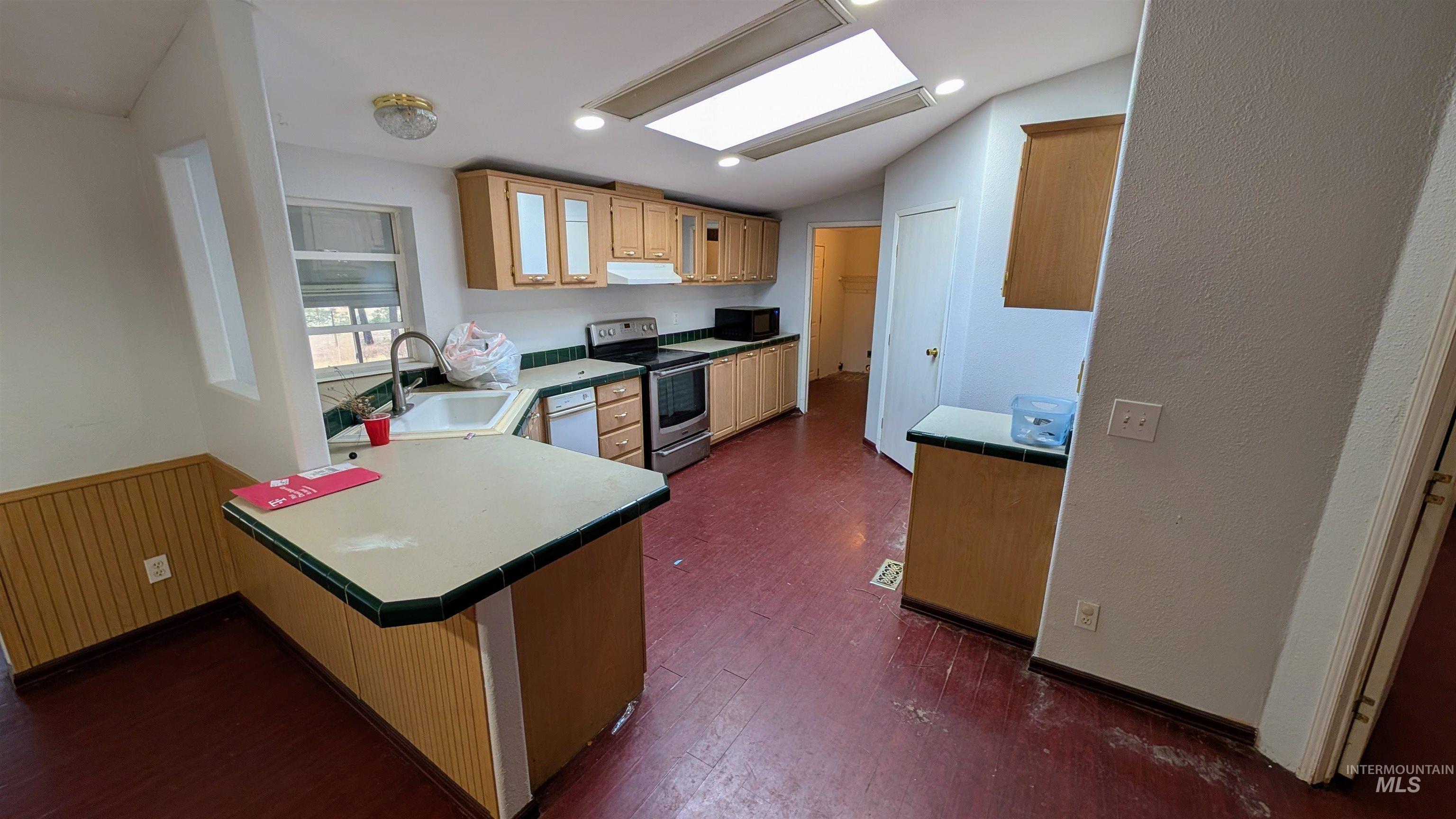 Kitchen with stainless steel range with electric stovetop, vaulted ceiling, a peninsula, light brown cabinets, and dark wood finished floors
