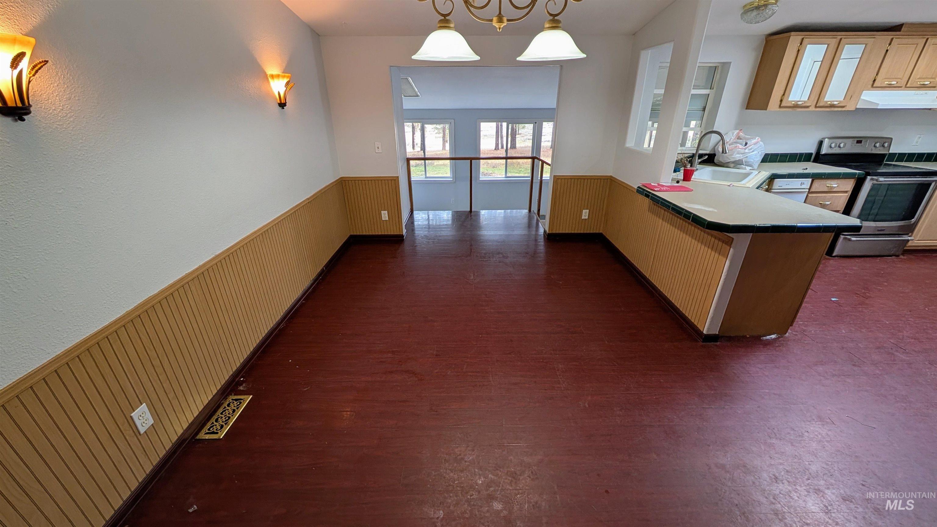 Kitchen with wainscoting, electric stove, a peninsula, hanging light fixtures, and dark wood-style floors
