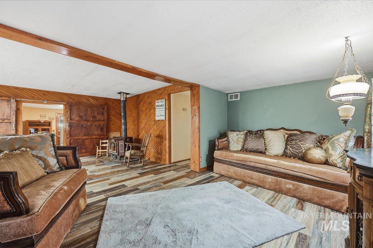Living room with a wood stove, wood walls, wood finished floors, and a textured ceiling