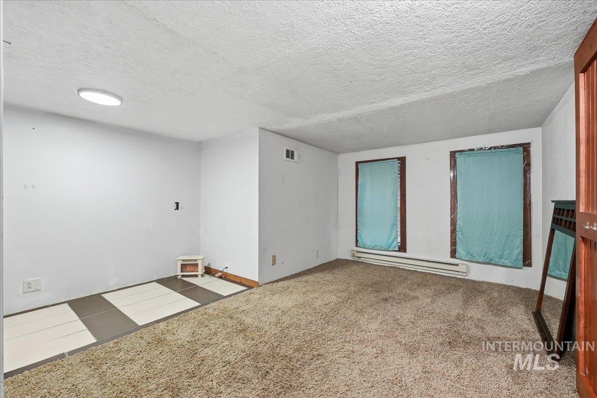 Carpeted empty room featuring a textured ceiling and a baseboard radiator