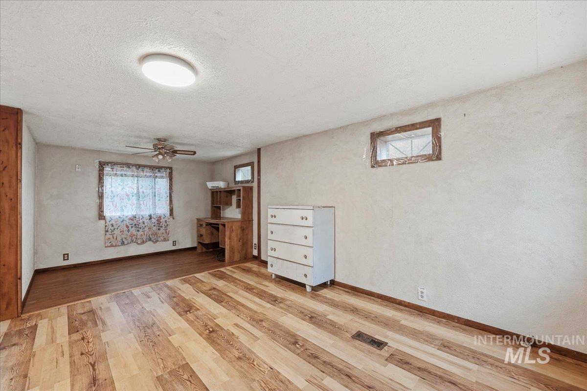 Unfurnished bedroom featuring light wood-type flooring, a textured ceiling, a textured wall, and a ceiling fan