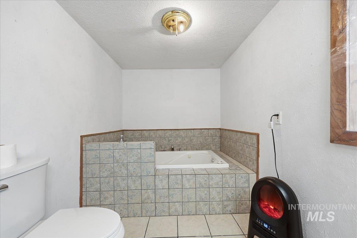 Full bathroom featuring a garden tub, a textured ceiling, tile patterned floors, and a textured wall