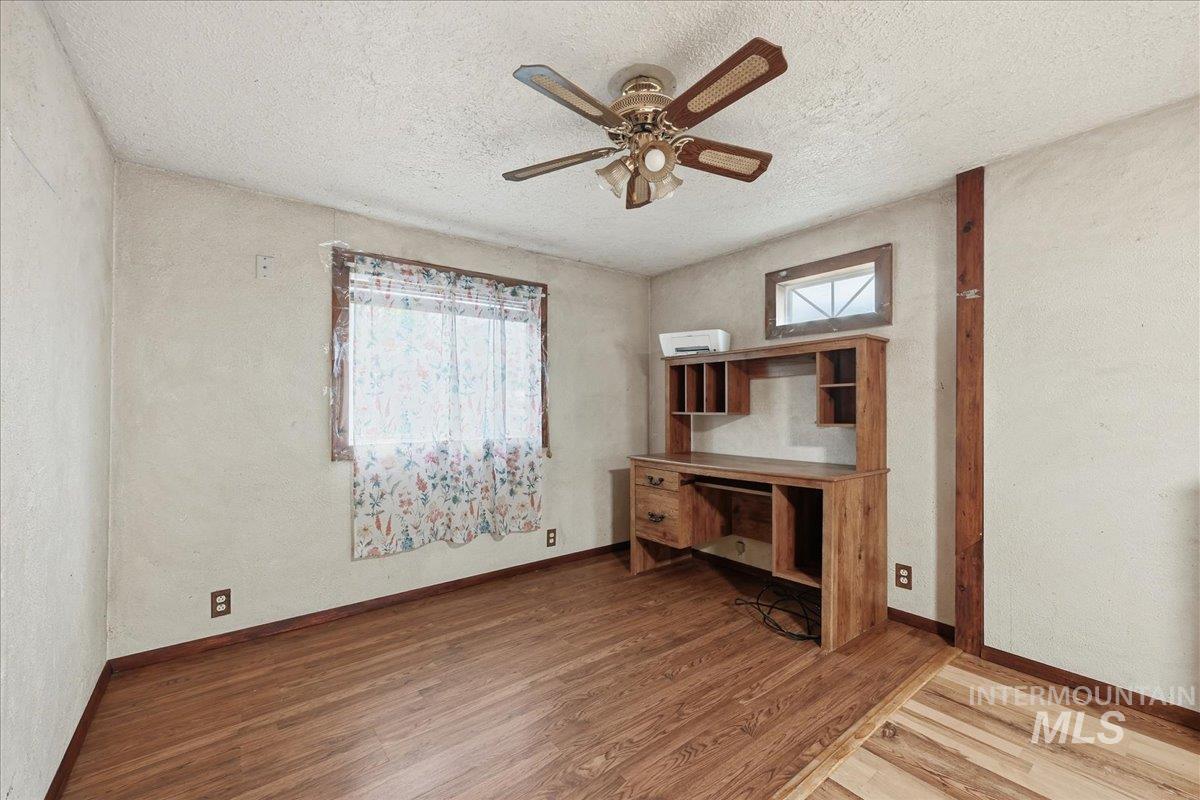 Unfurnished office with light wood-type flooring, a textured wall, healthy amount of natural light, a textured ceiling, and a ceiling fan