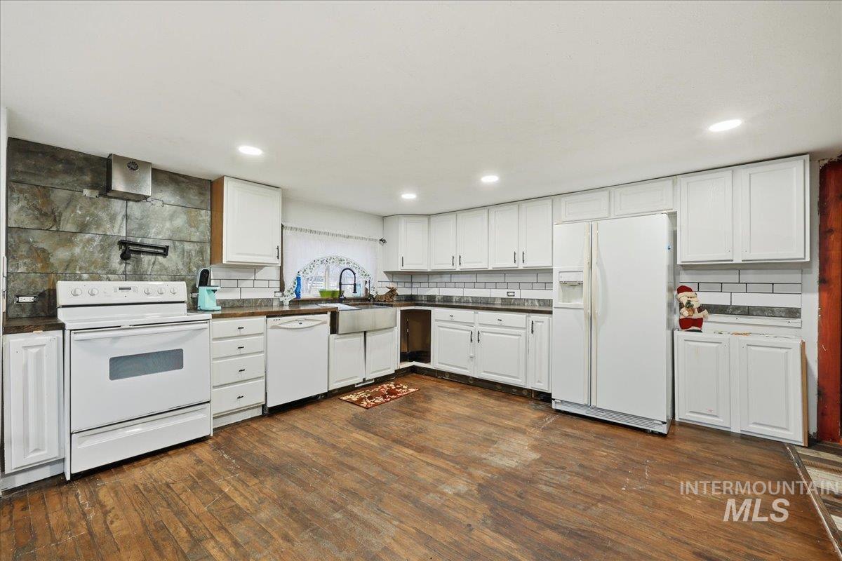 Kitchen featuring white cabinets, white appliances, dark countertops, and dark wood-type flooring