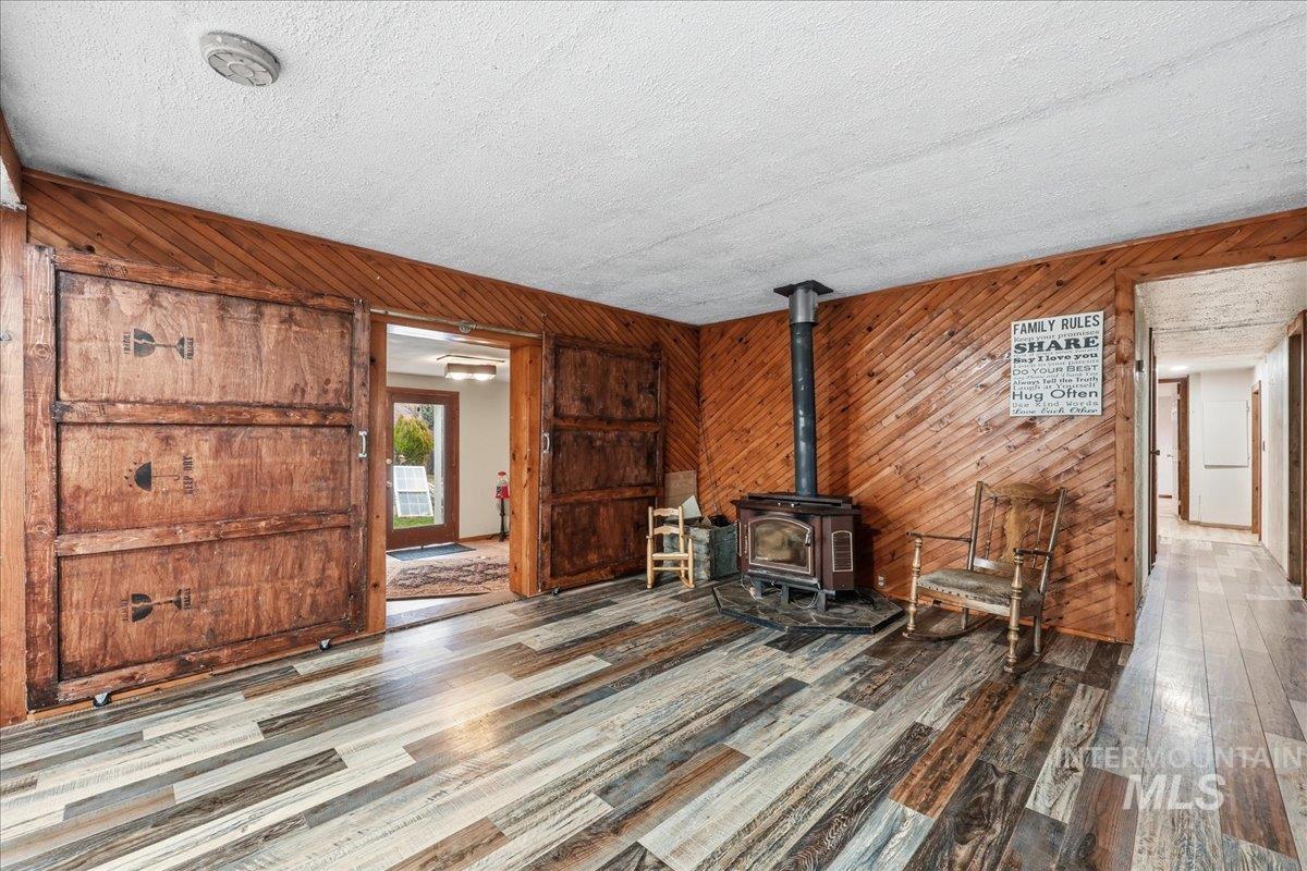 Unfurnished living room with a wood stove, wood walls, a textured ceiling, and wood finished floors