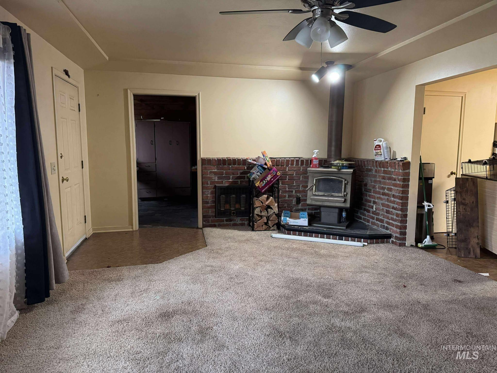 Living area featuring a wood stove, carpet flooring, and ceiling fan