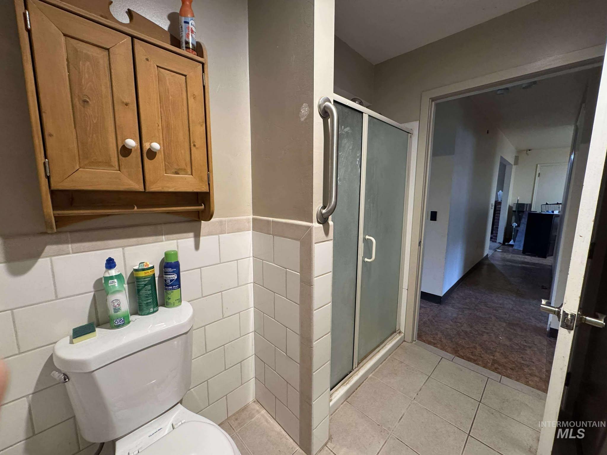 Bathroom featuring a shower stall, light tile patterned flooring, and wainscoting