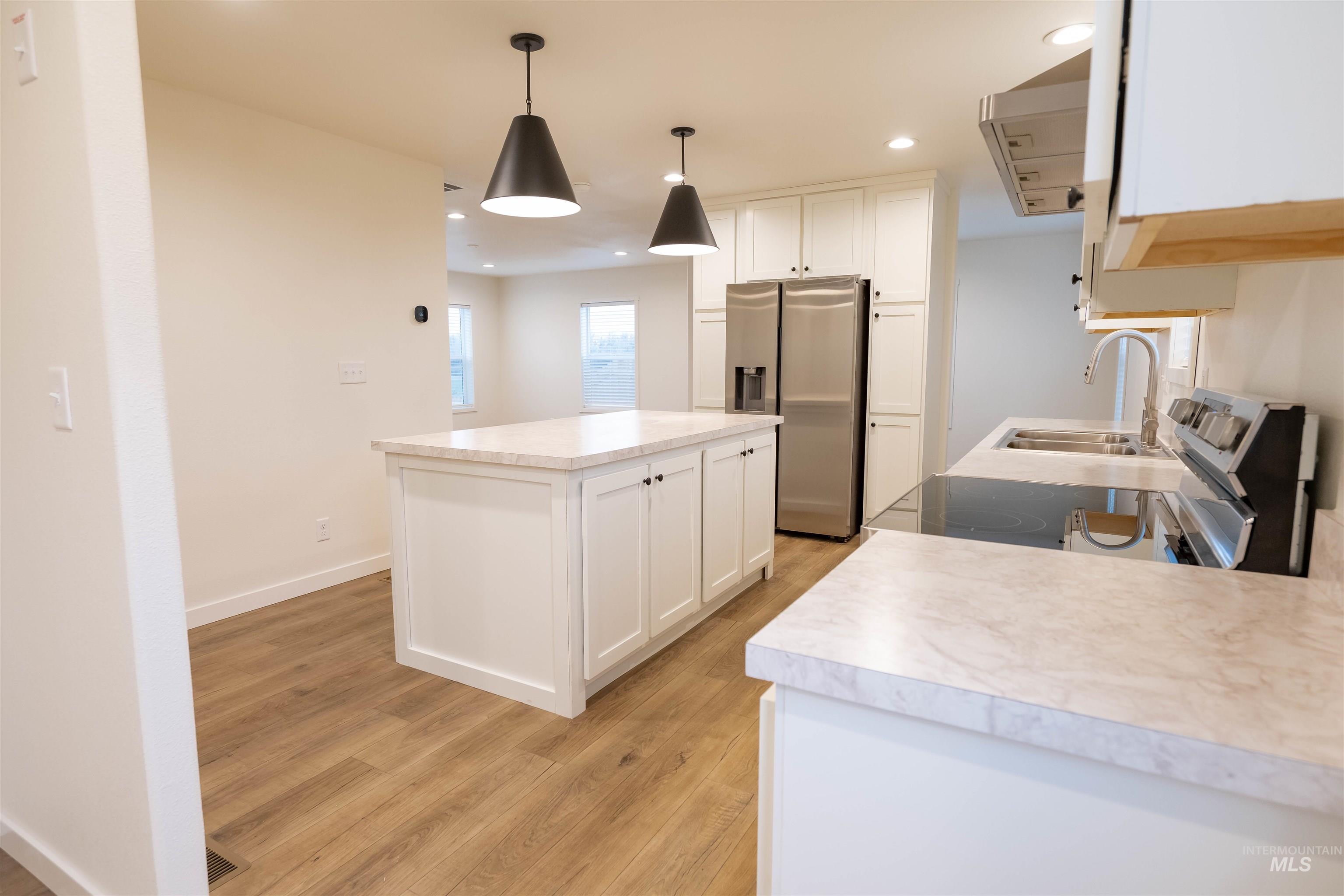 Kitchen with stainless steel appliances, white cabinetry, light countertops, range hood, and a kitchen island
