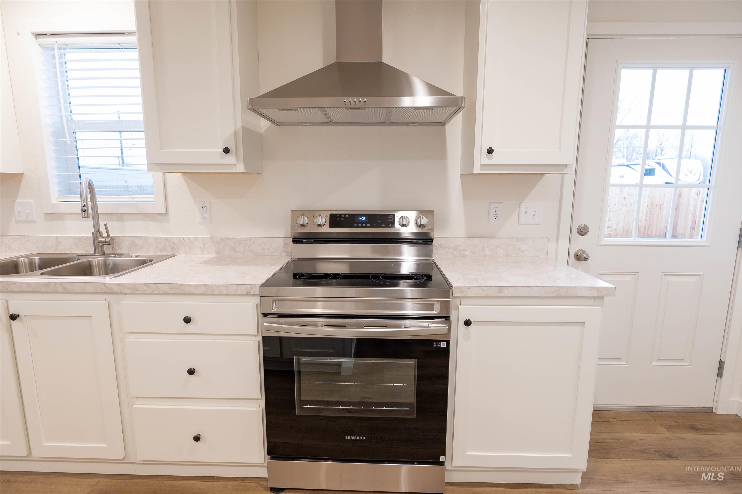 Kitchen with stainless steel range with electric cooktop, wall chimney exhaust hood, plenty of natural light, and light countertops