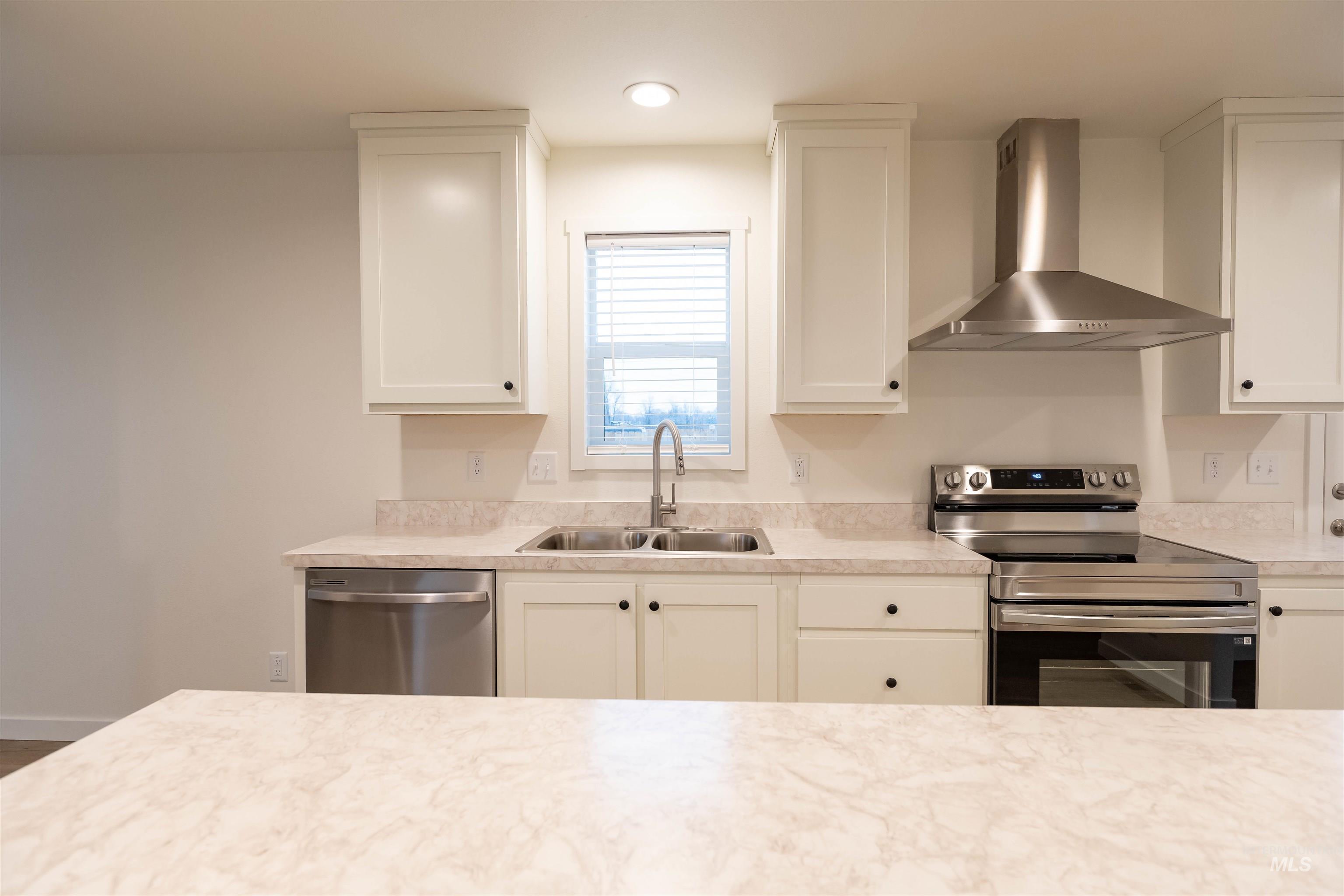 Kitchen with stainless steel appliances, wall chimney exhaust hood, light countertops, and white cabinets