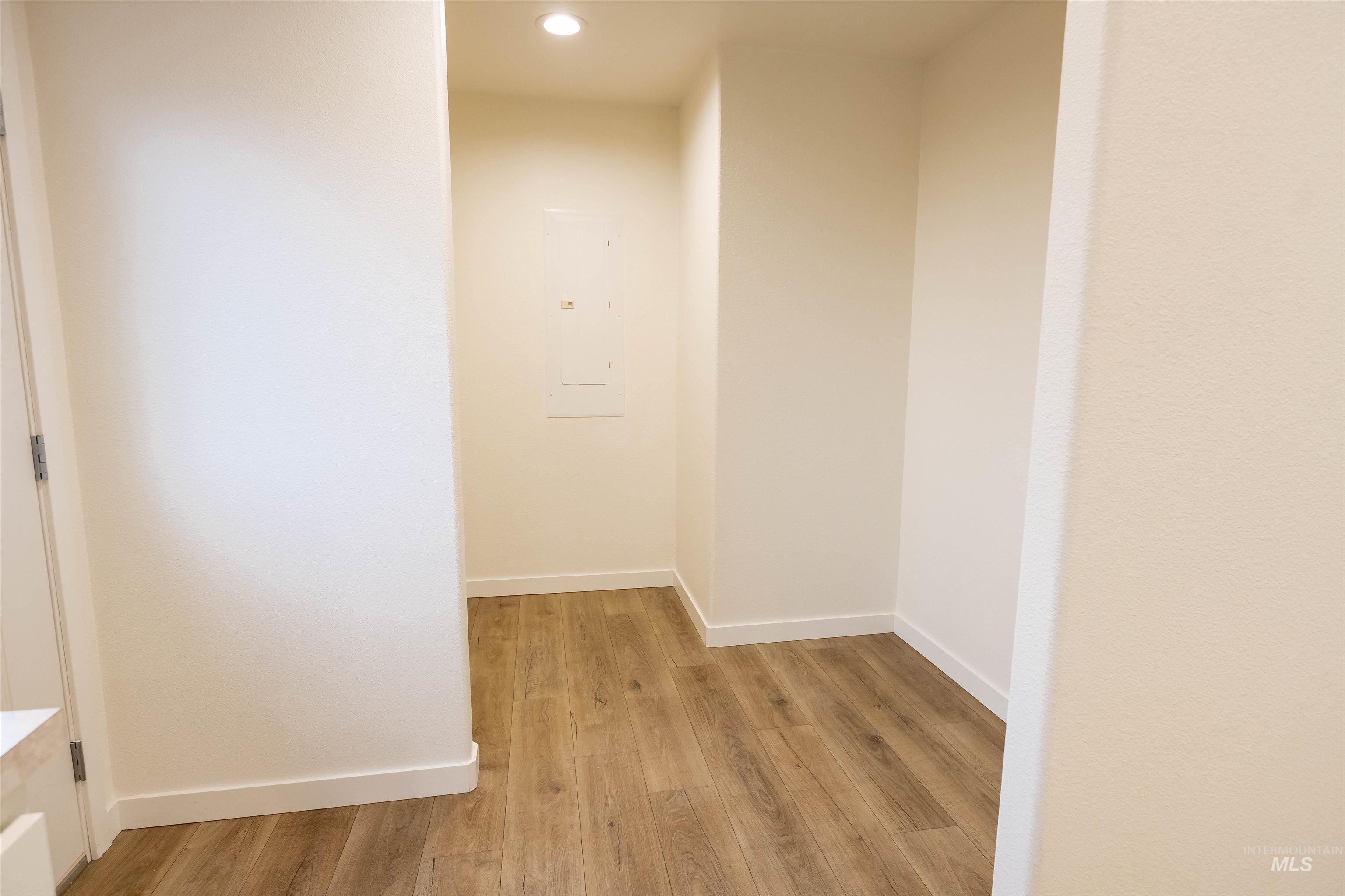 Hall with light wood-style flooring, electric panel, and recessed lighting