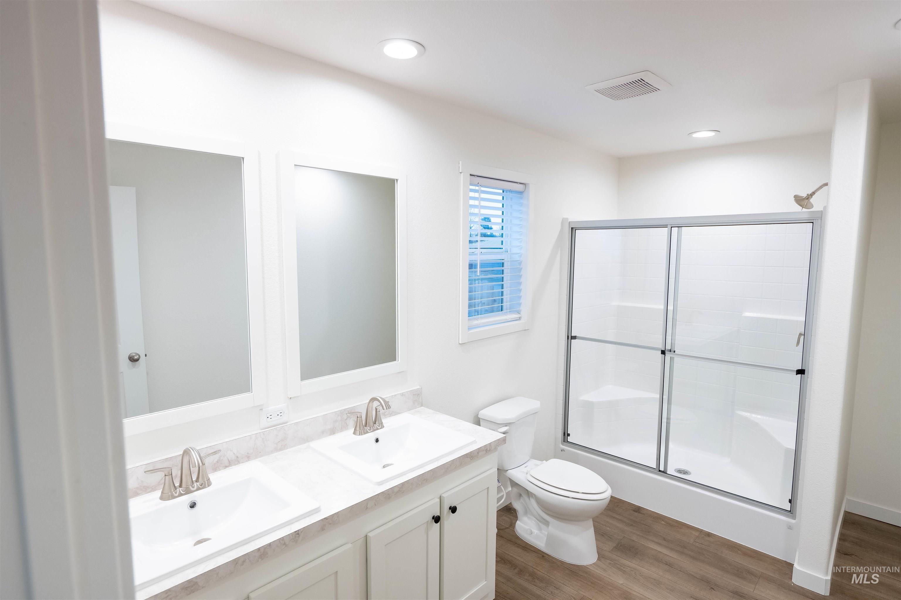 Bathroom featuring dark wood-style flooring, double vanity, a stall shower, and recessed lighting