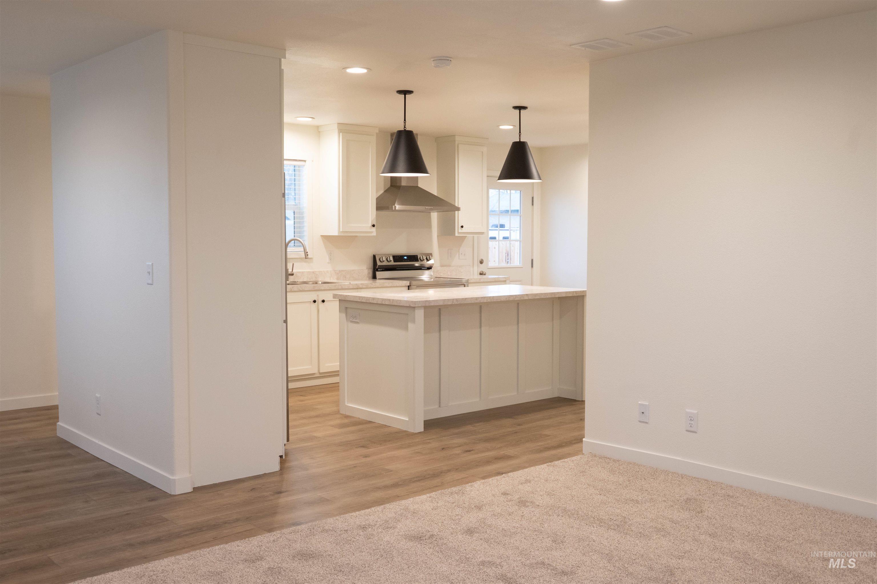 Kitchen with hanging light fixtures, electric stove, white cabinetry, wall chimney exhaust hood, and light wood-style flooring