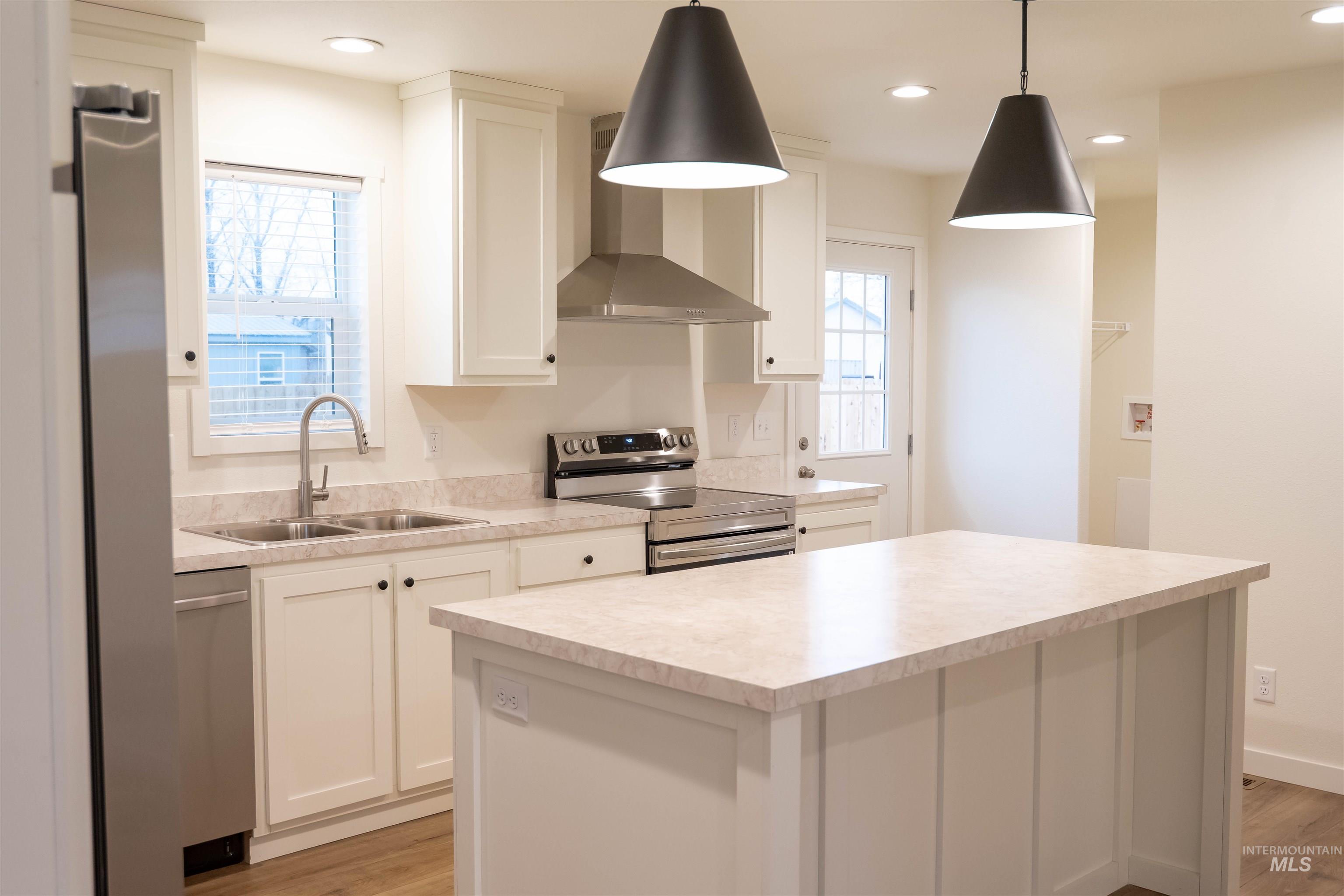Kitchen with stainless steel appliances, wall chimney range hood, light countertops, a center island, and white cabinetry