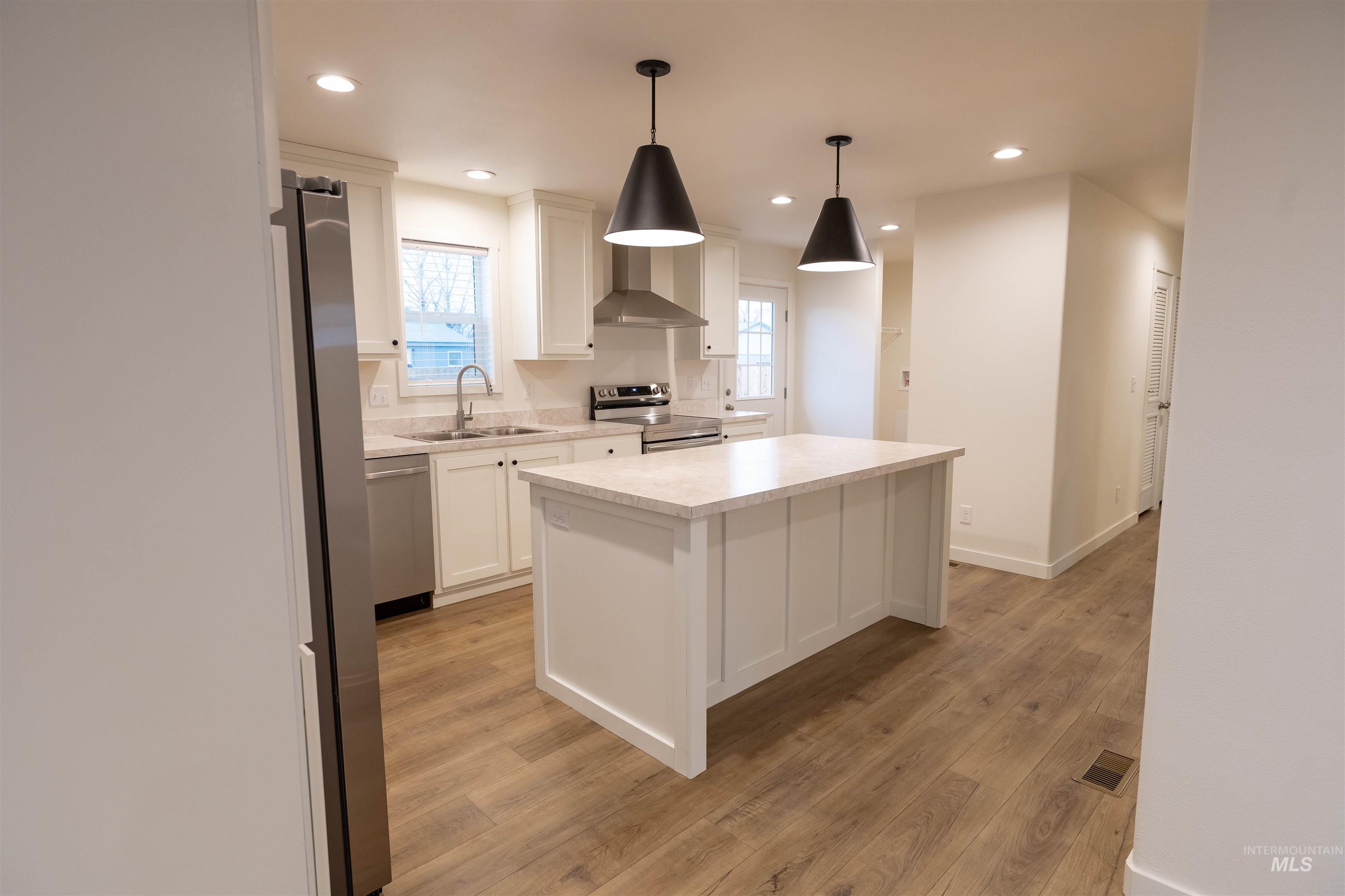Kitchen with a kitchen island, light countertops, wall chimney exhaust hood, stainless steel appliances, and light wood-style flooring