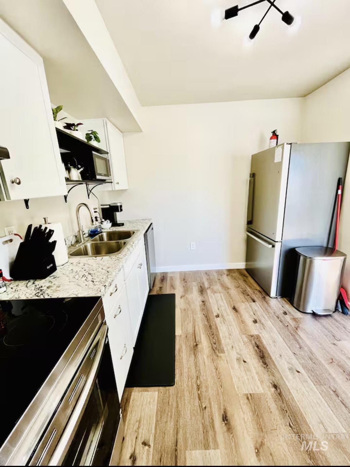 Kitchen featuring stainless steel appliances, white cabinets, light wood-style flooring, and light stone counters