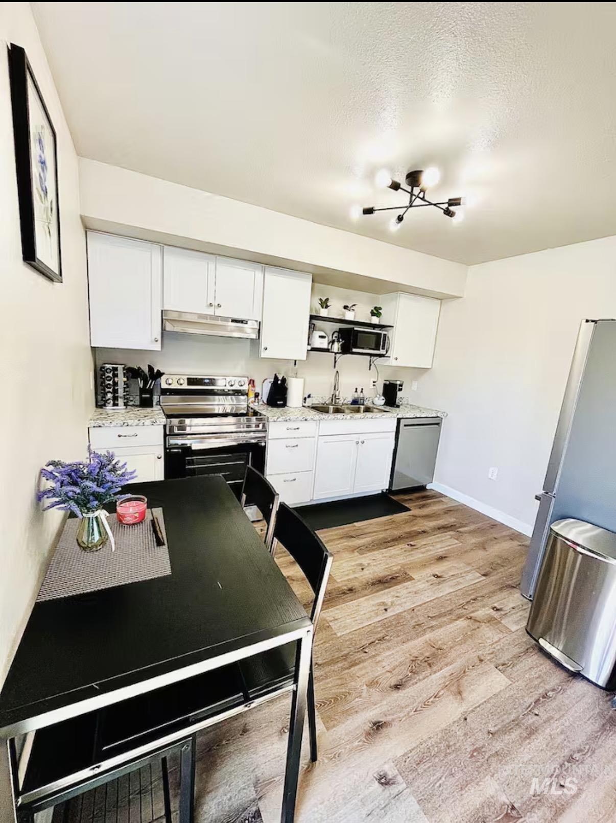 Kitchen with stainless steel appliances, white cabinets, open shelves, under cabinet range hood, and light wood finished floors