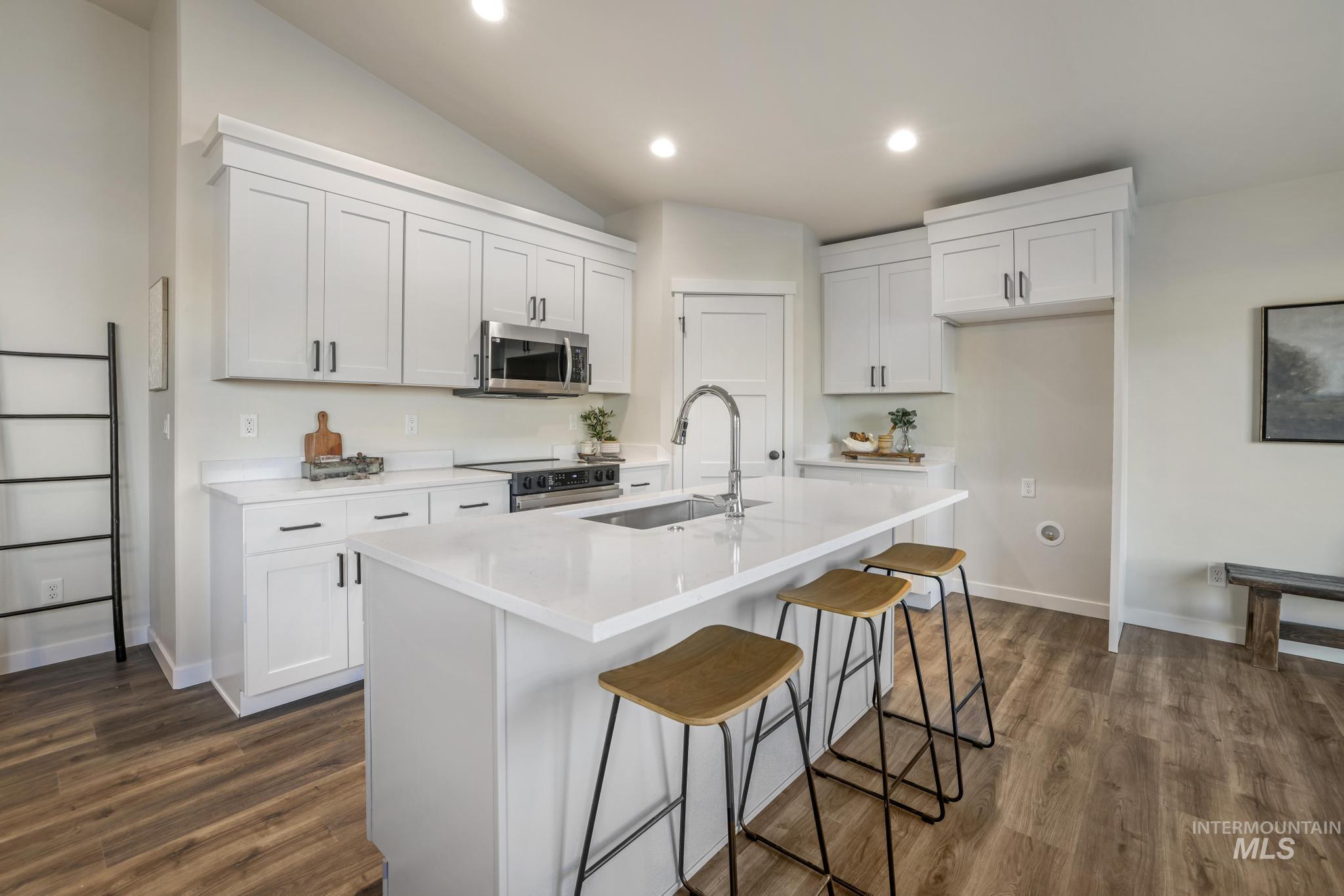 Kitchen featuring a kitchen bar, white cabinets, vaulted ceiling, appliances with stainless steel finishes, and a center island with sink
