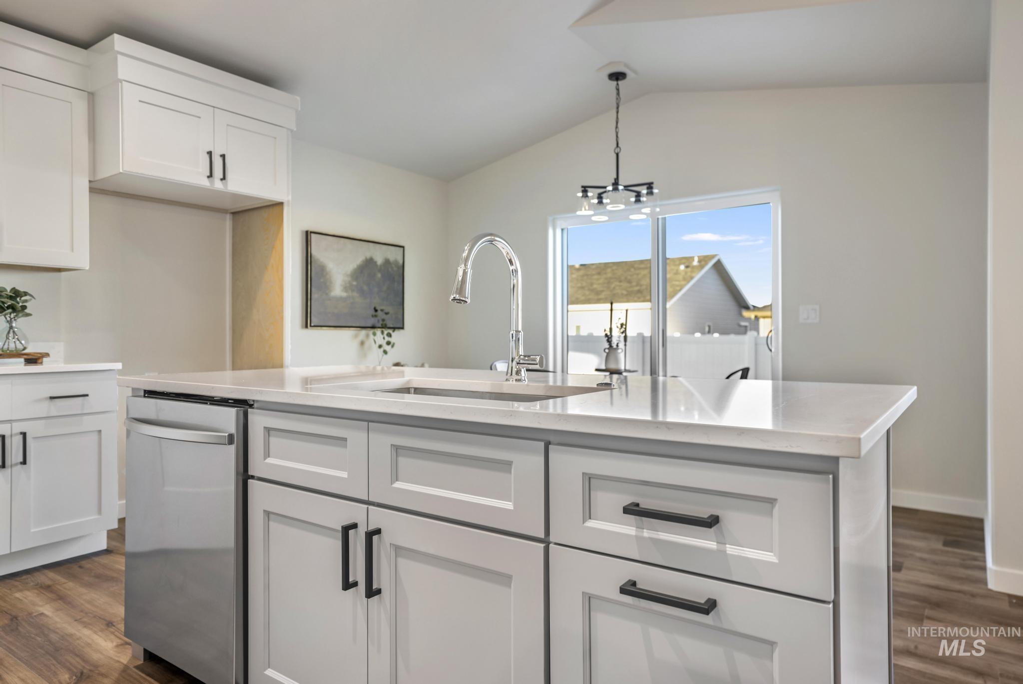 Kitchen with white cabinets, dark wood-style flooring, stainless steel dishwasher, an island with sink, and vaulted ceiling