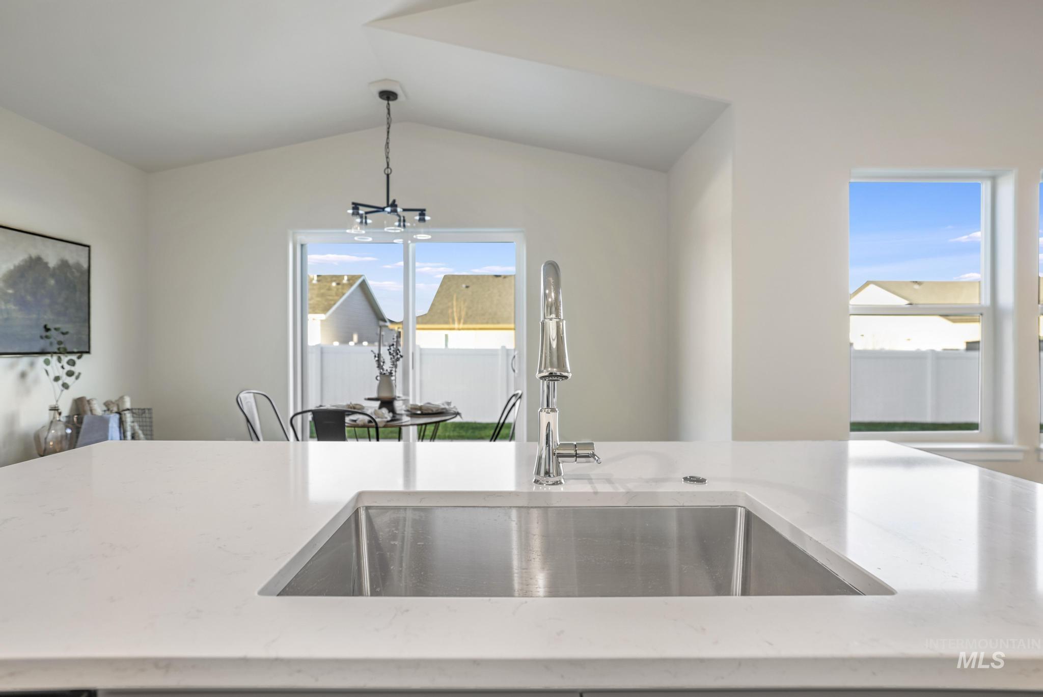 Kitchen featuring light stone counters, vaulted ceiling, and hanging light fixtures