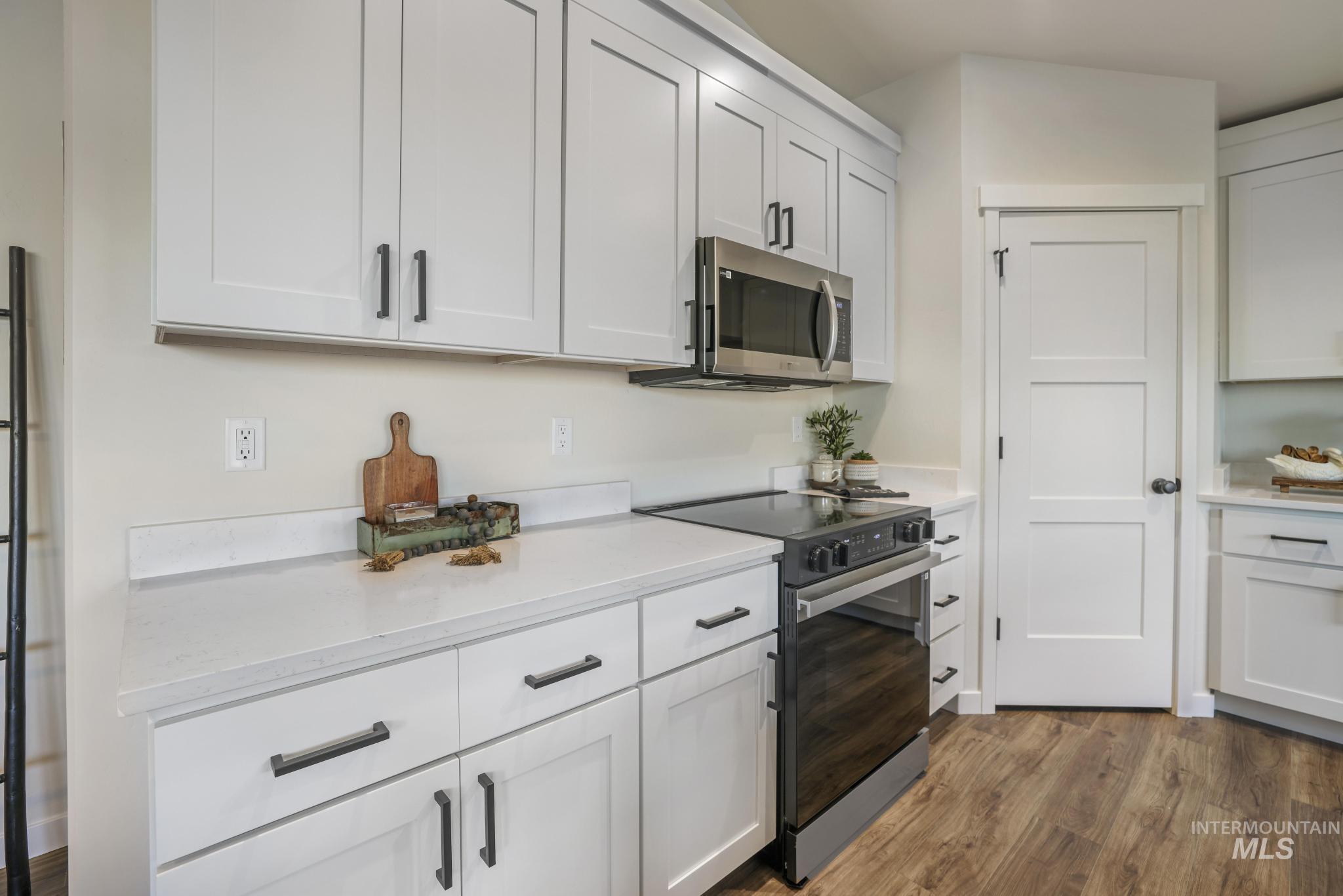 Kitchen featuring black range with electric cooktop, stainless steel microwave, dark wood-type flooring, and white cabinets