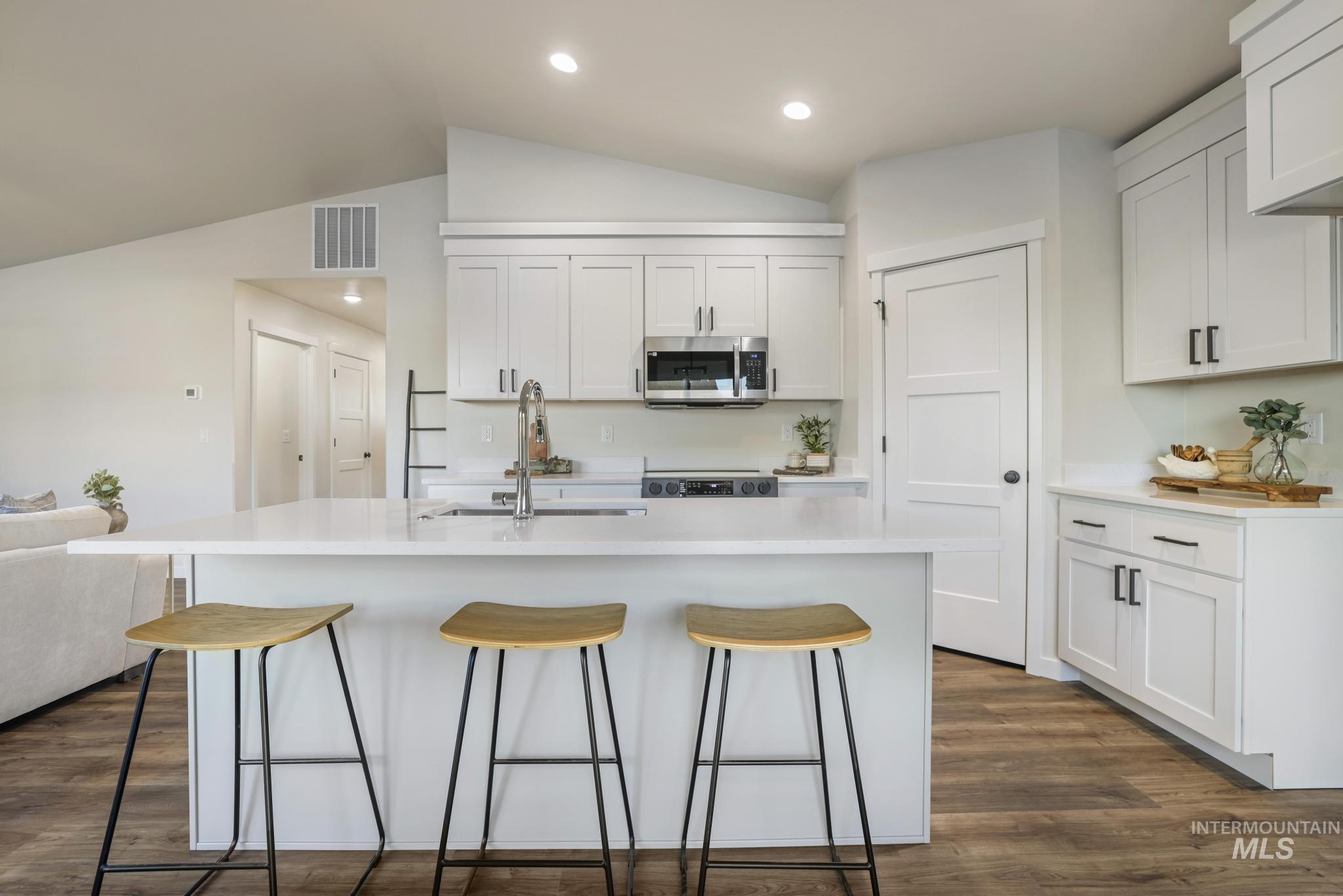 Kitchen with vaulted ceiling, dark wood-type flooring, white cabinets, a breakfast bar, and stainless steel microwave