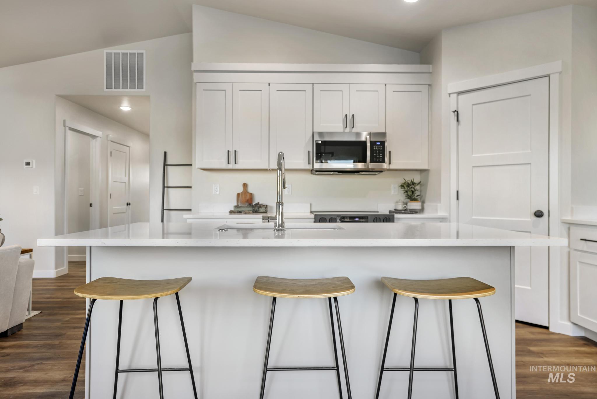 Kitchen featuring dark wood-style floors, white cabinets, stainless steel microwave, vaulted ceiling, and recessed lighting