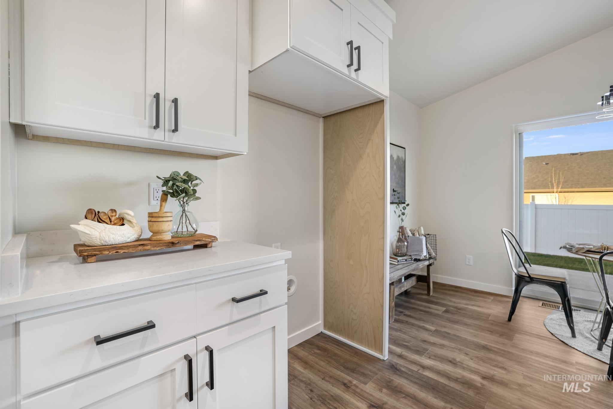 Kitchen with white cabinetry, light stone counters, lofted ceiling, and dark wood-style flooring