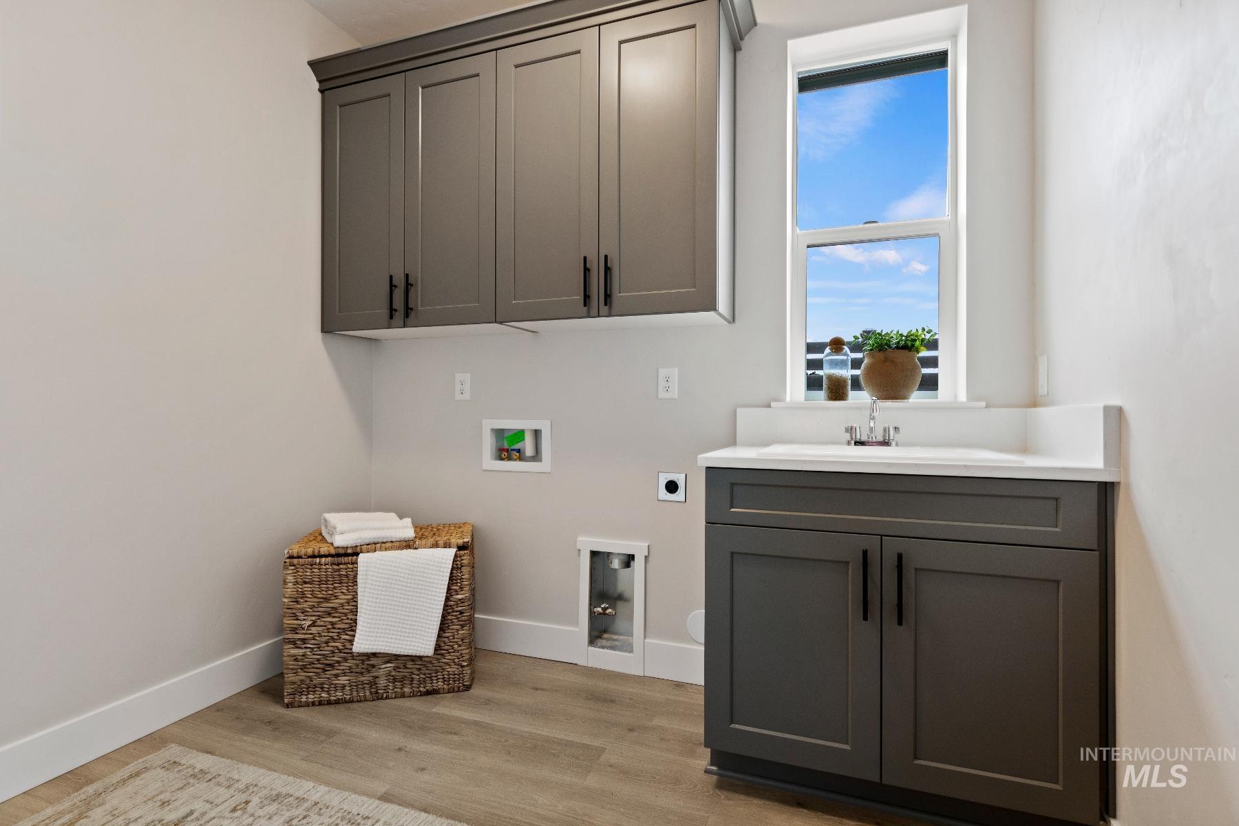 Laundry area featuring electric dryer hookup, washer hookup, light wood-type flooring, and cabinet space