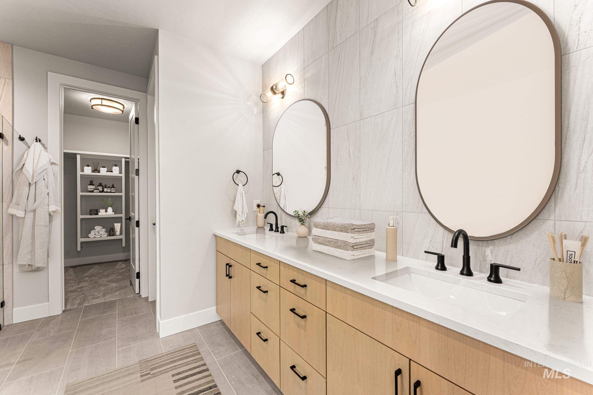 Full bathroom with double vanity, light tile patterned floors, tile walls, and a walk in closet