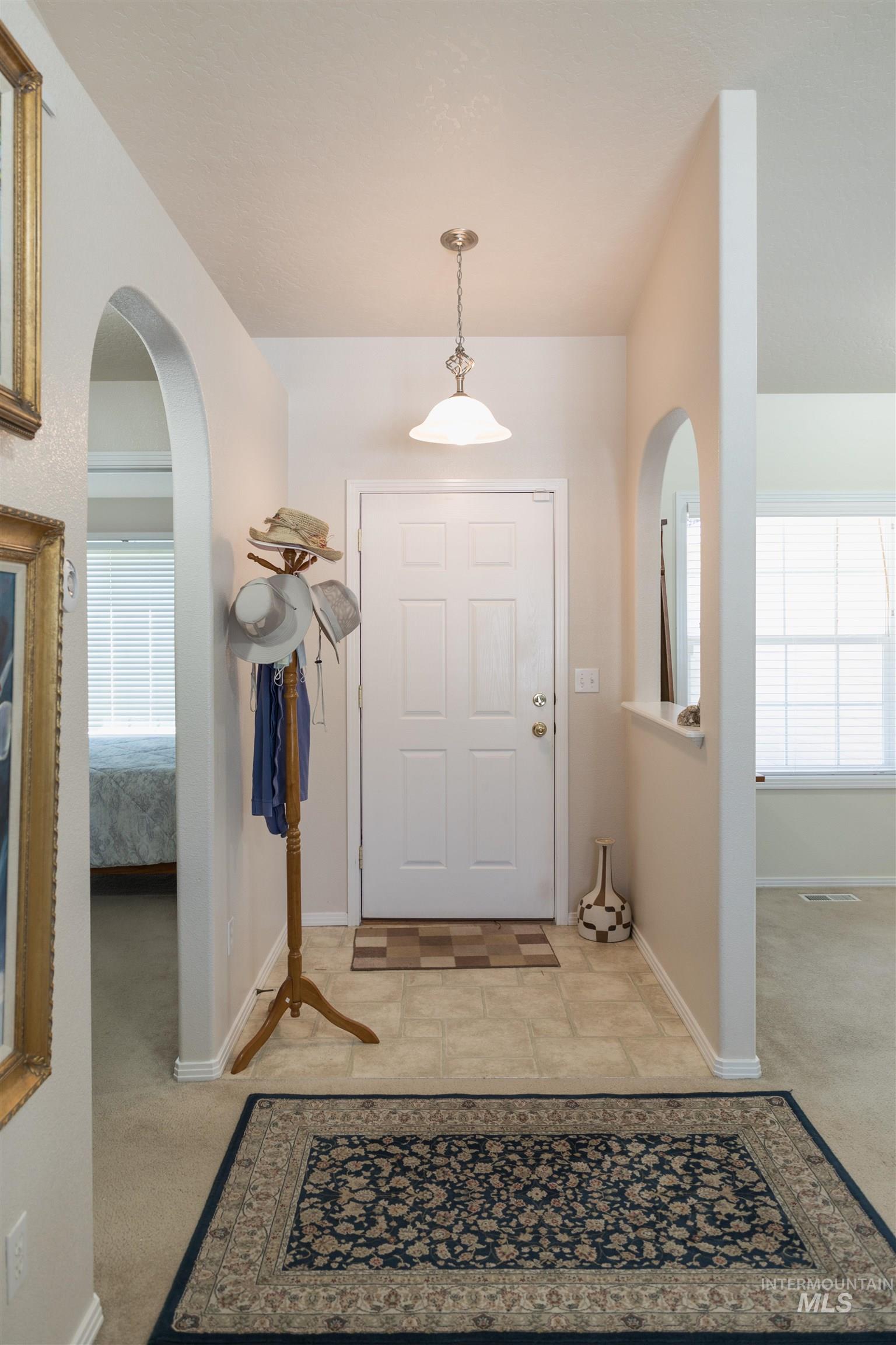 Foyer featuring arched walkways, light carpet, and stone tile floors