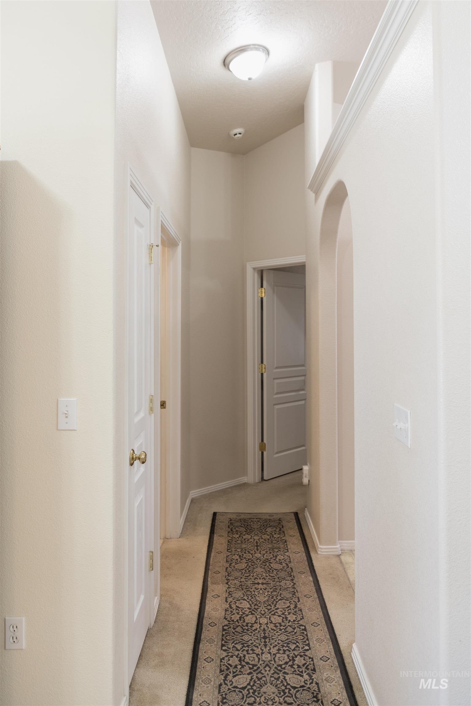 Hallway featuring light colored carpet, arched walkways, and a textured ceiling