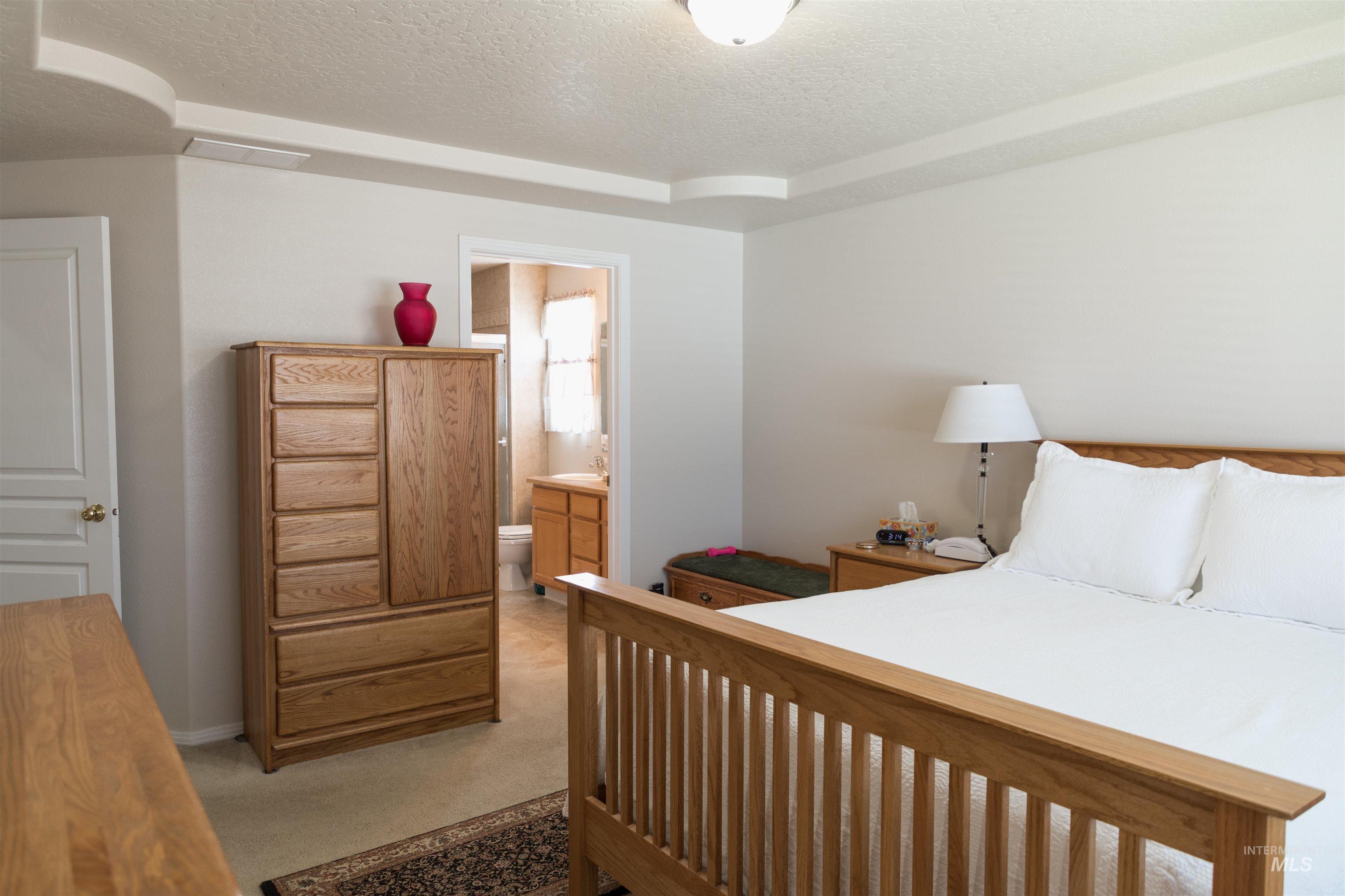 Bedroom featuring a textured ceiling, light colored carpet, and connected bathroom