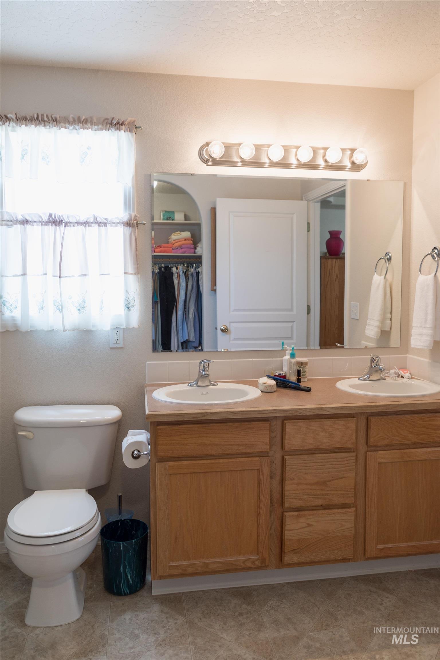 Bathroom featuring double vanity, a textured ceiling, and light tile patterned flooring