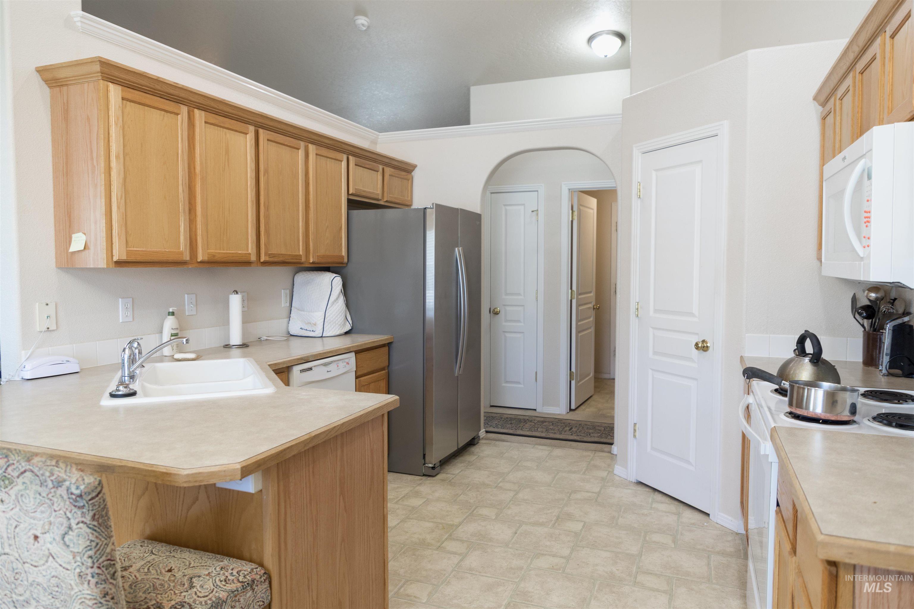 Kitchen with light countertops, white appliances, a breakfast bar area, a peninsula, and stone finish floors