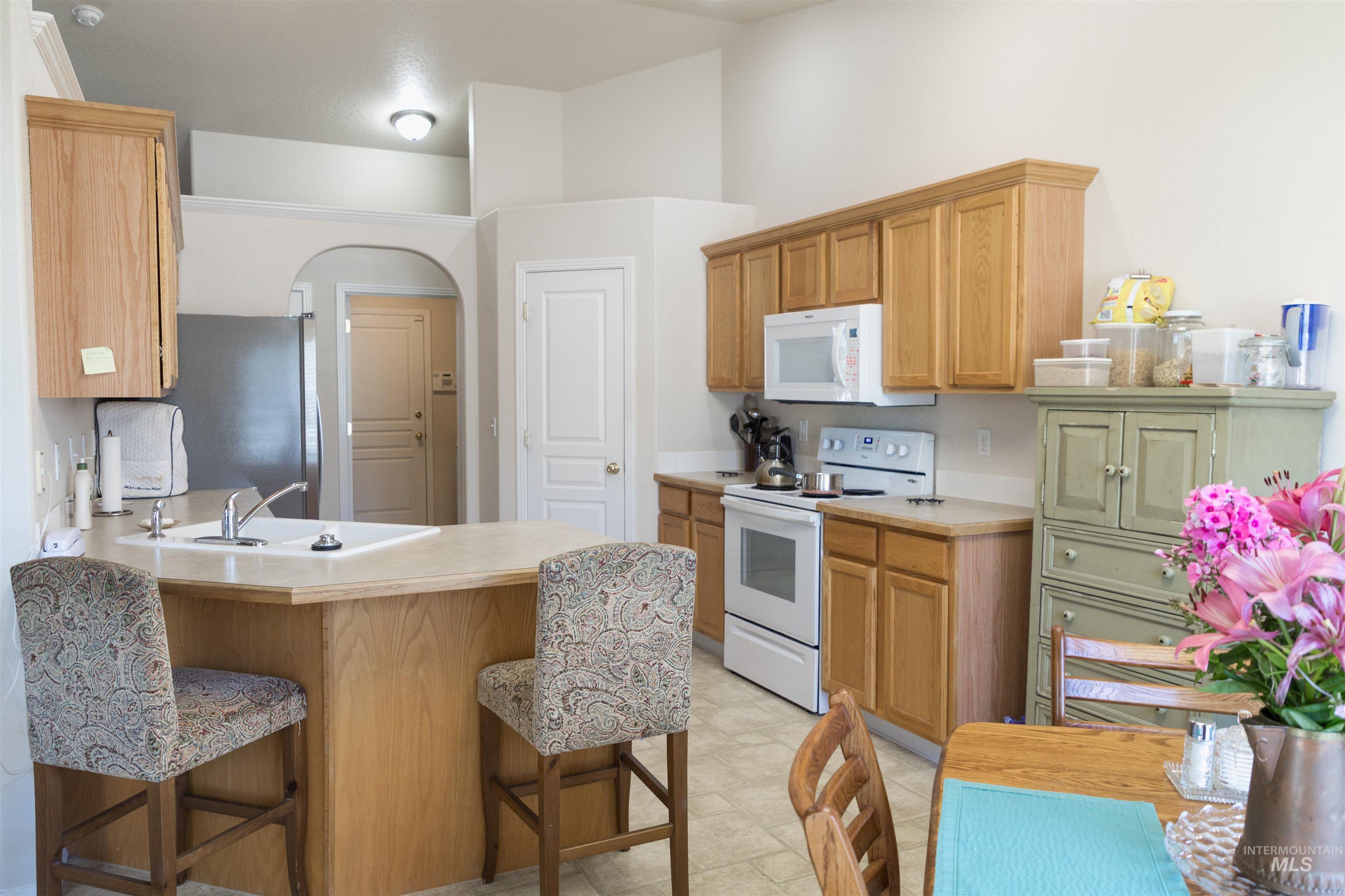 Kitchen featuring a breakfast bar, white appliances, light countertops, arched walkways, and a peninsula