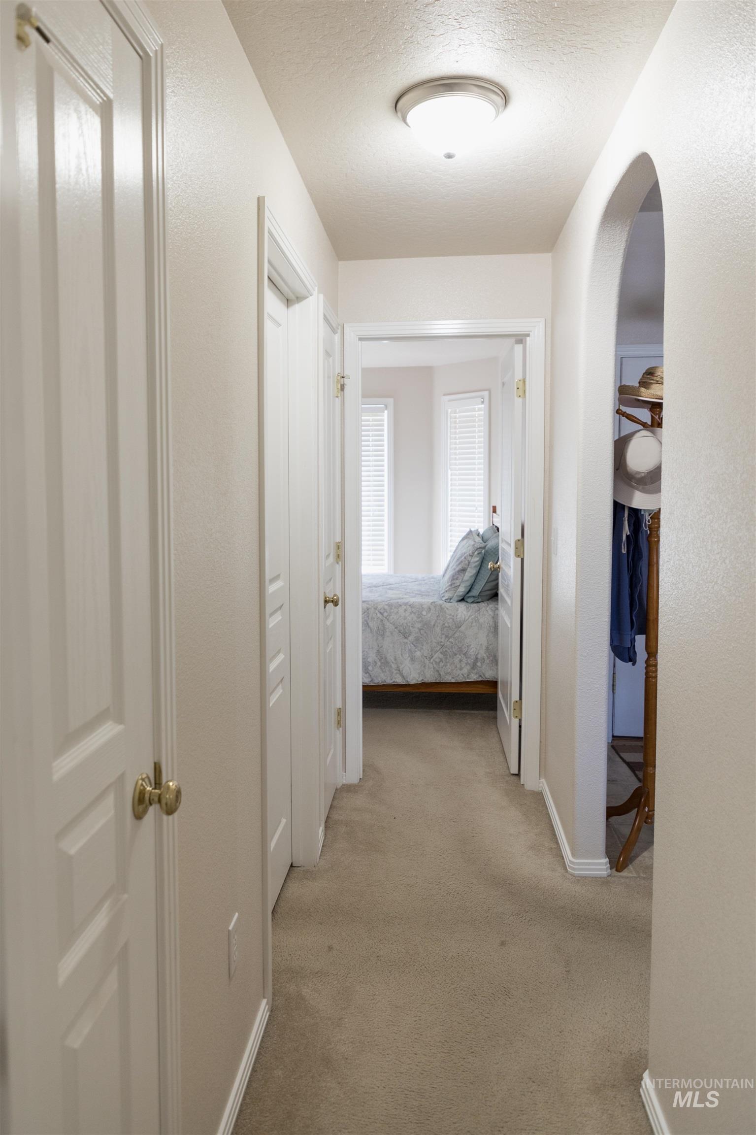 Hall featuring light colored carpet, arched walkways, and a textured ceiling
