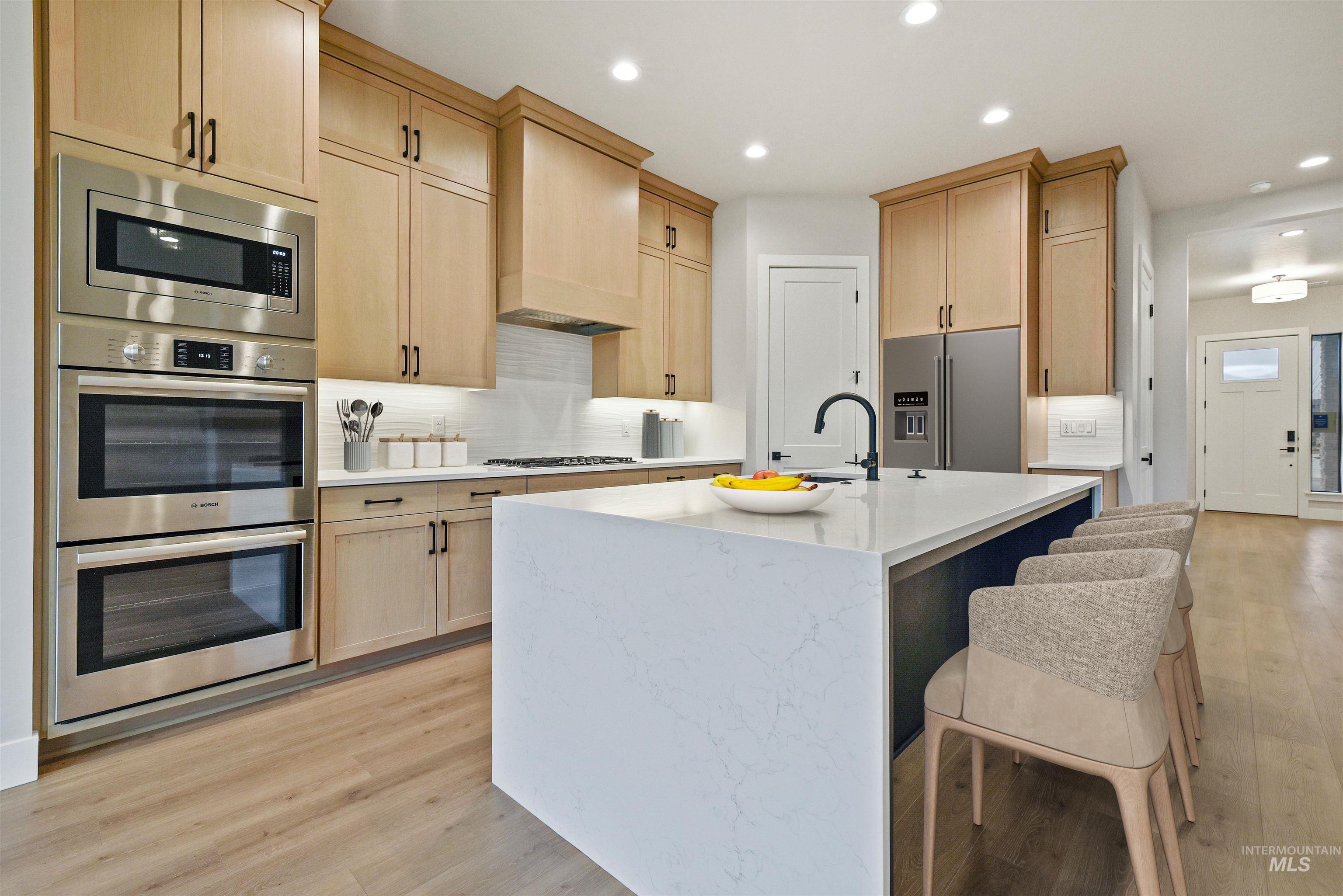 Kitchen with light brown cabinetry, stainless steel appliances, light stone counters, a kitchen bar, and recessed lighting