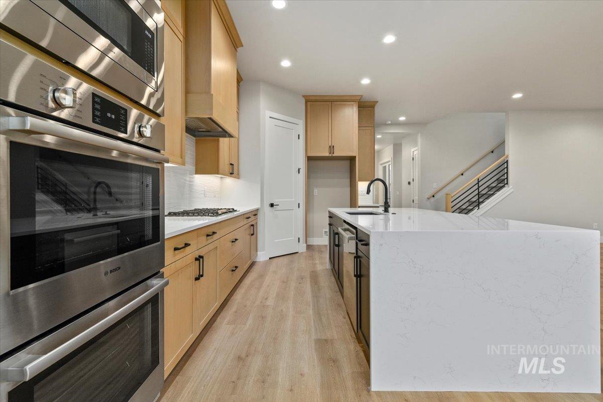 Kitchen with appliances with stainless steel finishes, light stone countertops, recessed lighting, an island with sink, and light wood-style flooring